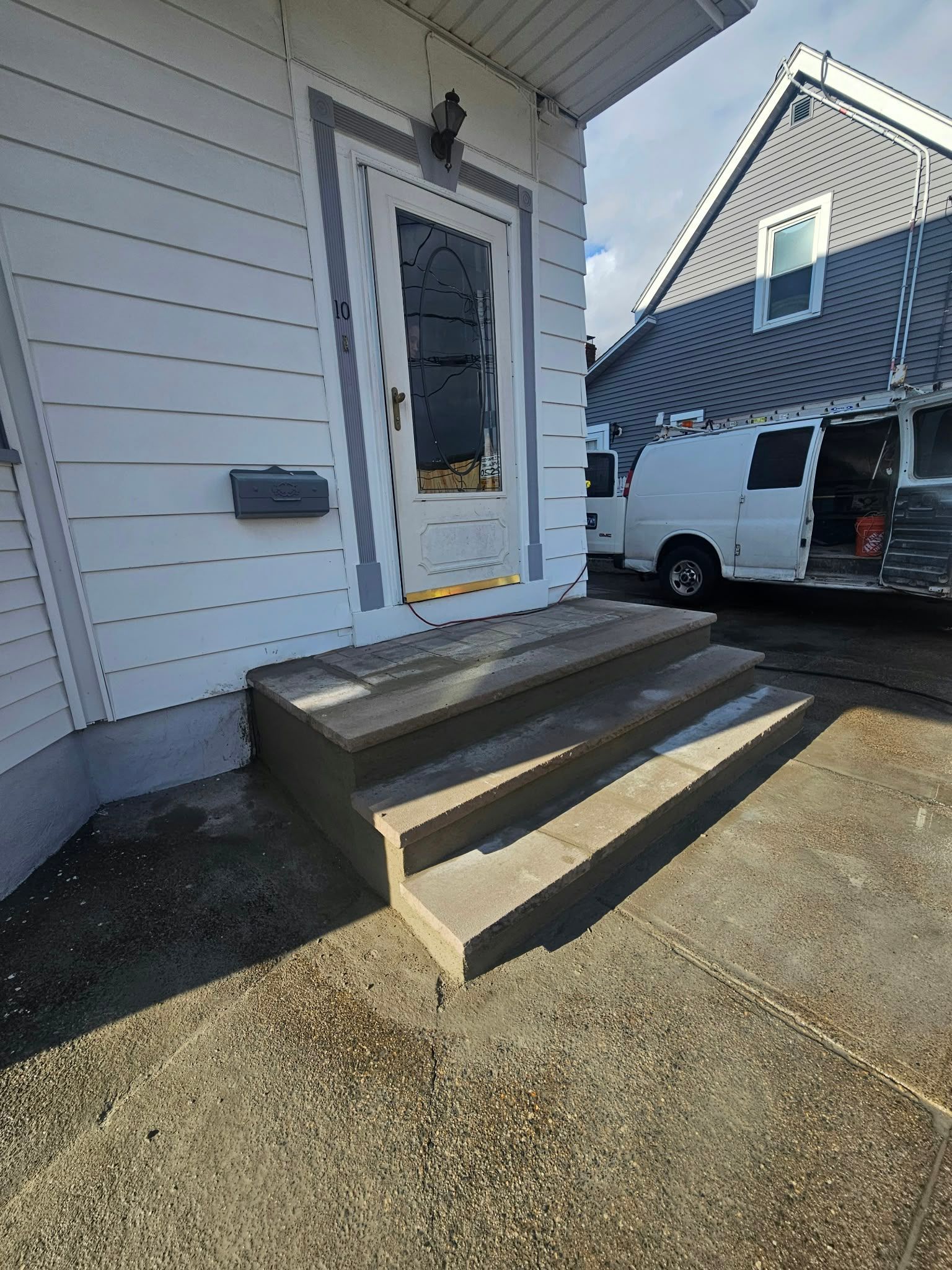 Front steps with a white door and a van parked beside a house under construction.