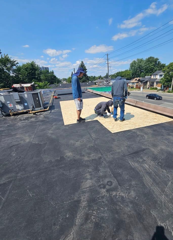 Workers installing roofing on a flat roof under a bright blue sky