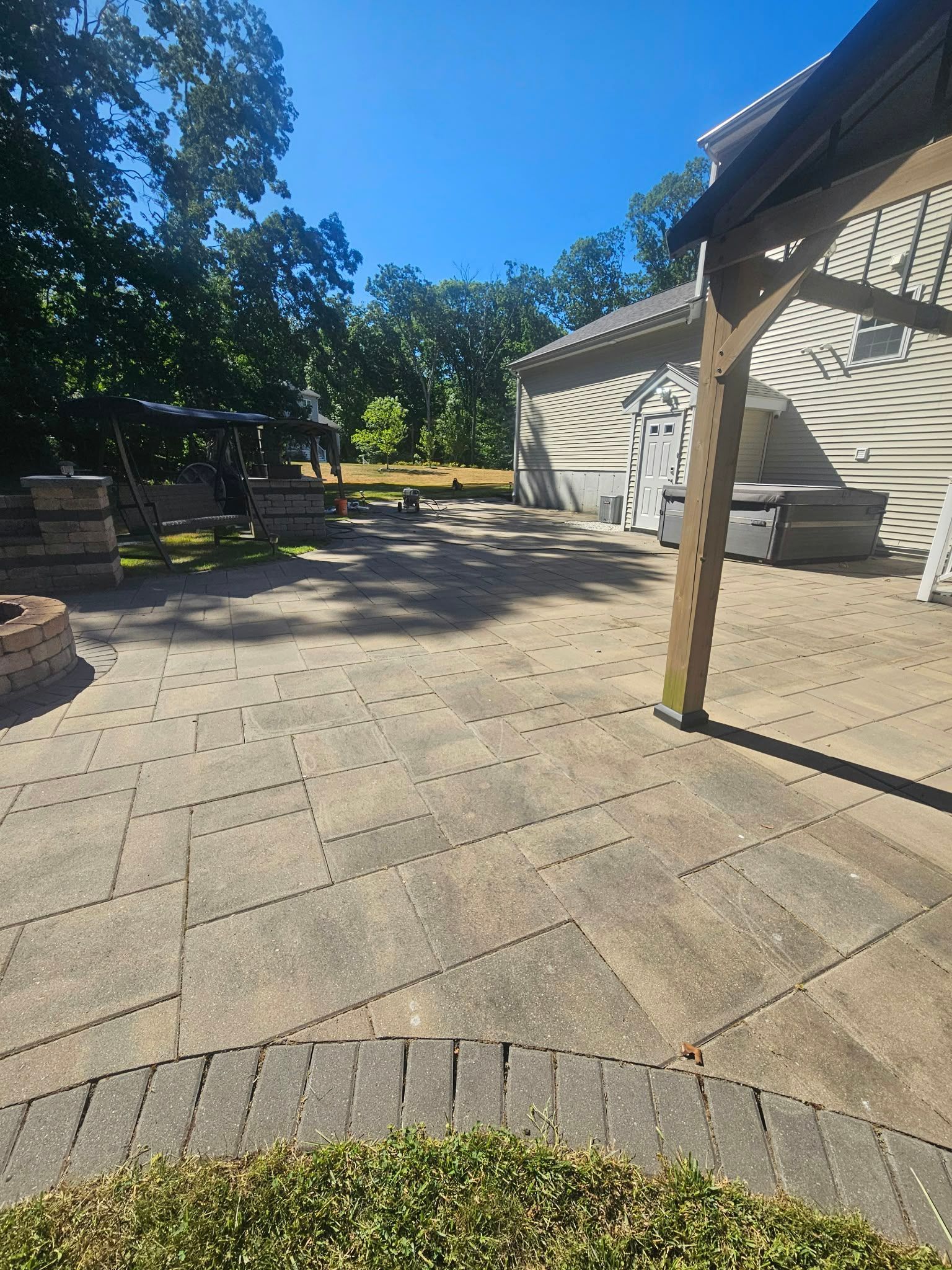 Sunlit stone patio with tables, benches, and a beige house under trees