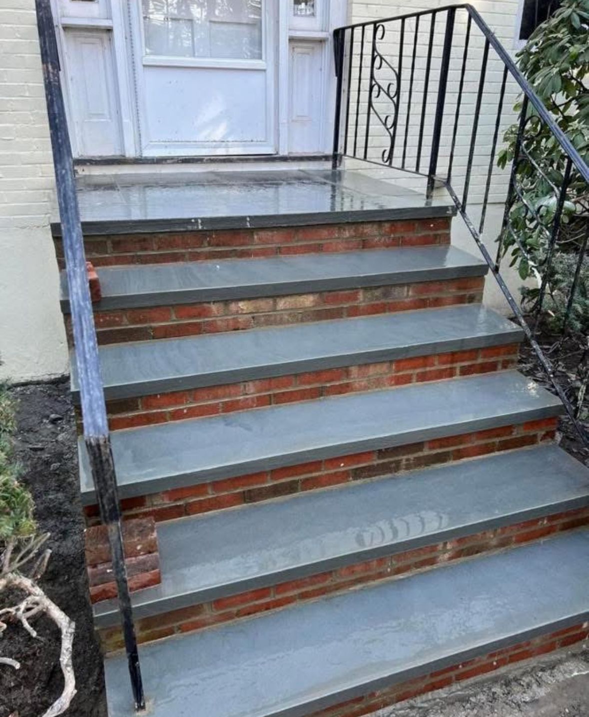 Front steps with gray concrete treads, red brick risers, and black metal railings leading to a white door
