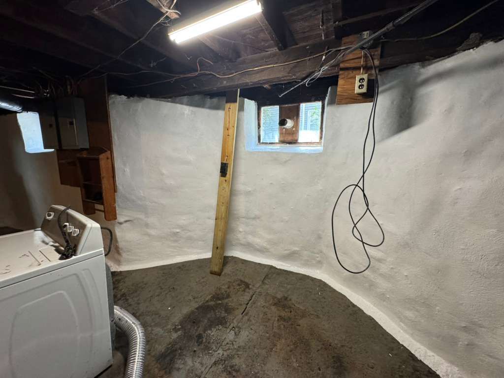 Unfinished basement with white walls, exposed ceiling, small windows, and a washer at left.