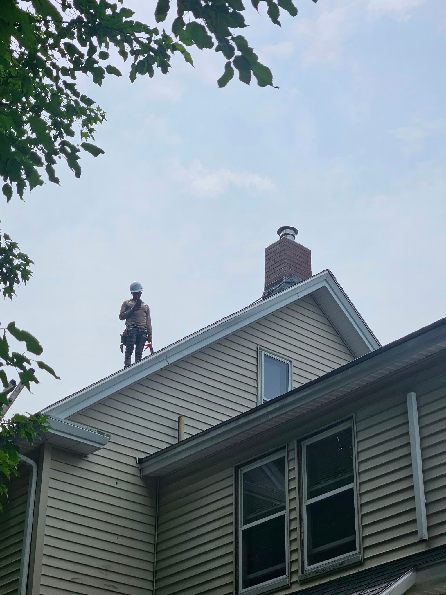 House roof with two small rooftop statues, chimney, and tree leaves against a cloudy sky
