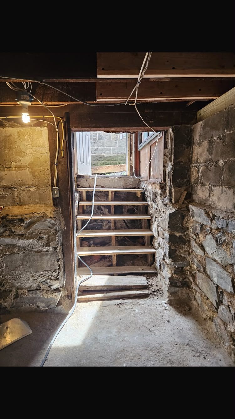 Dim basement stairway leading up to a bright doorway in a rough stone-walled room