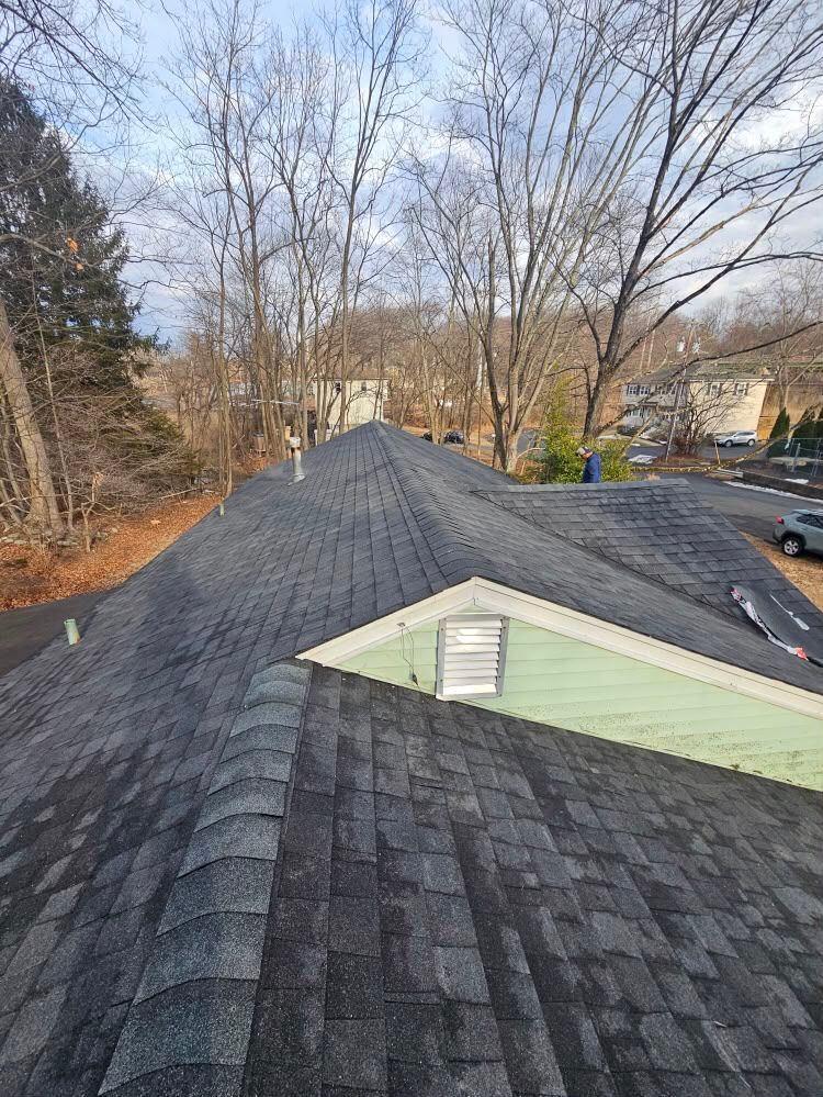 Roof shingles on a house under construction, with a chimney and leafless trees in the background.
