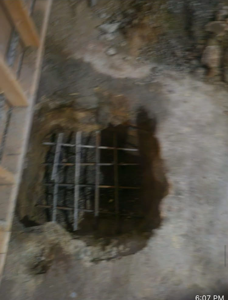 Broken concrete floor with a rebar-covered hole or drain opening exposed beneath.