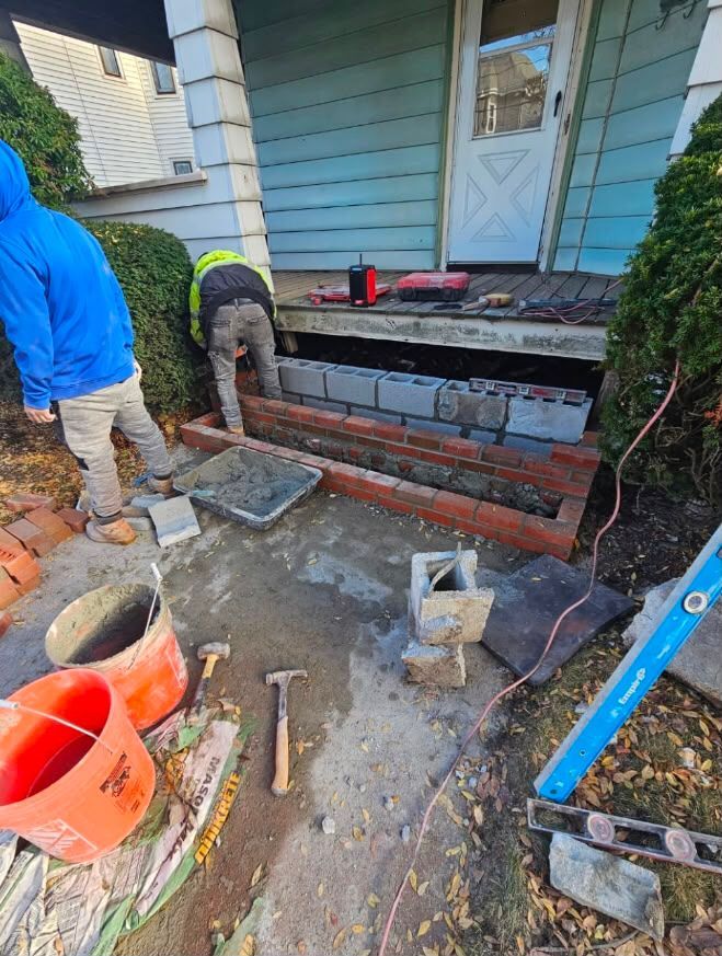 Workers rebuilding front steps and brick retaining wall at a house