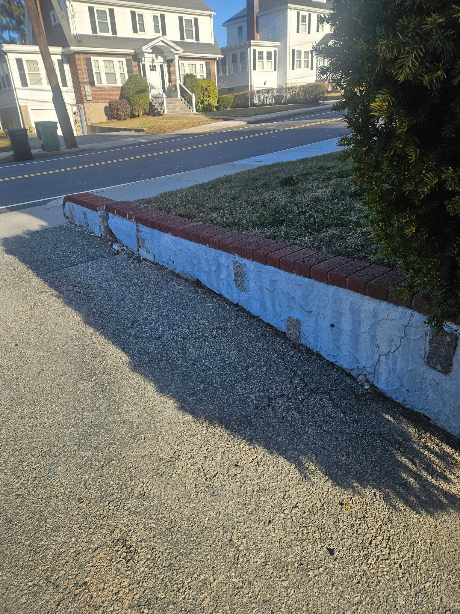 Gravel walkway beside a low white-and-red wall, with houses and a street in the background.