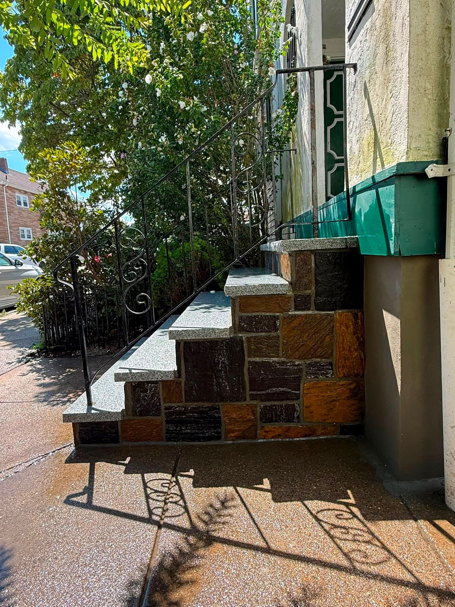 Tiled outdoor steps beside a building, with green awnings, trees, and sunlit pavement.