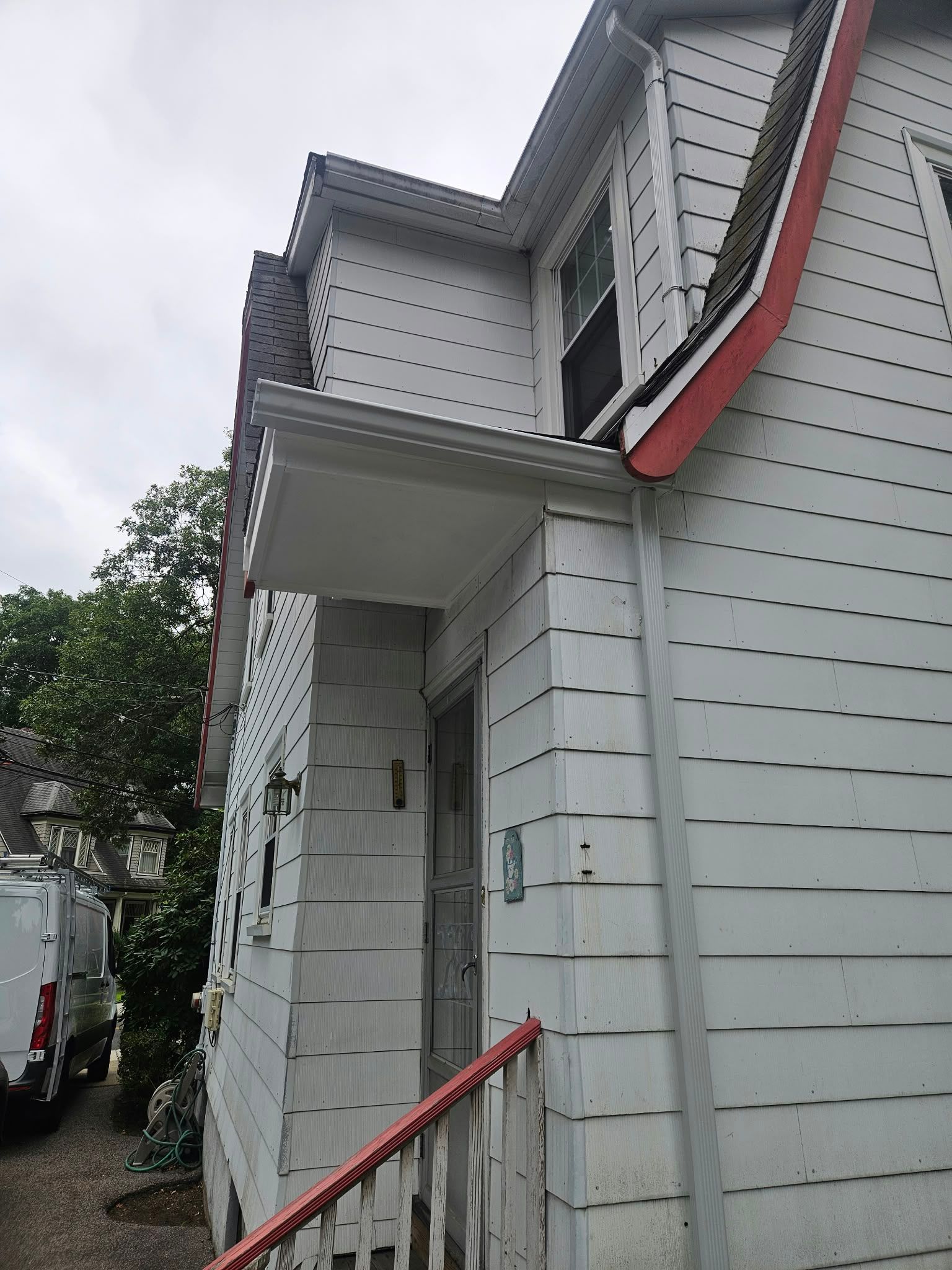 White house exterior with red-trimmed roof and a small front porch under a cloudy sky