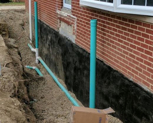 Blue pipes installed beside a brick house foundation during construction work