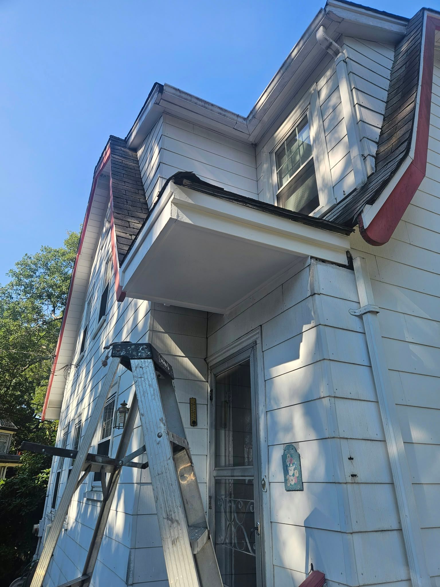 White house exterior with peeling paint, ladder, and covered porch viewed from below