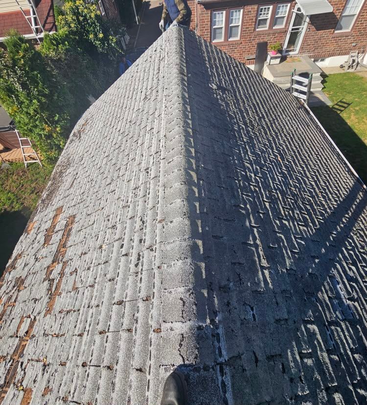 Aerial view of a weathered gray tiled roof between brick houses and green yards