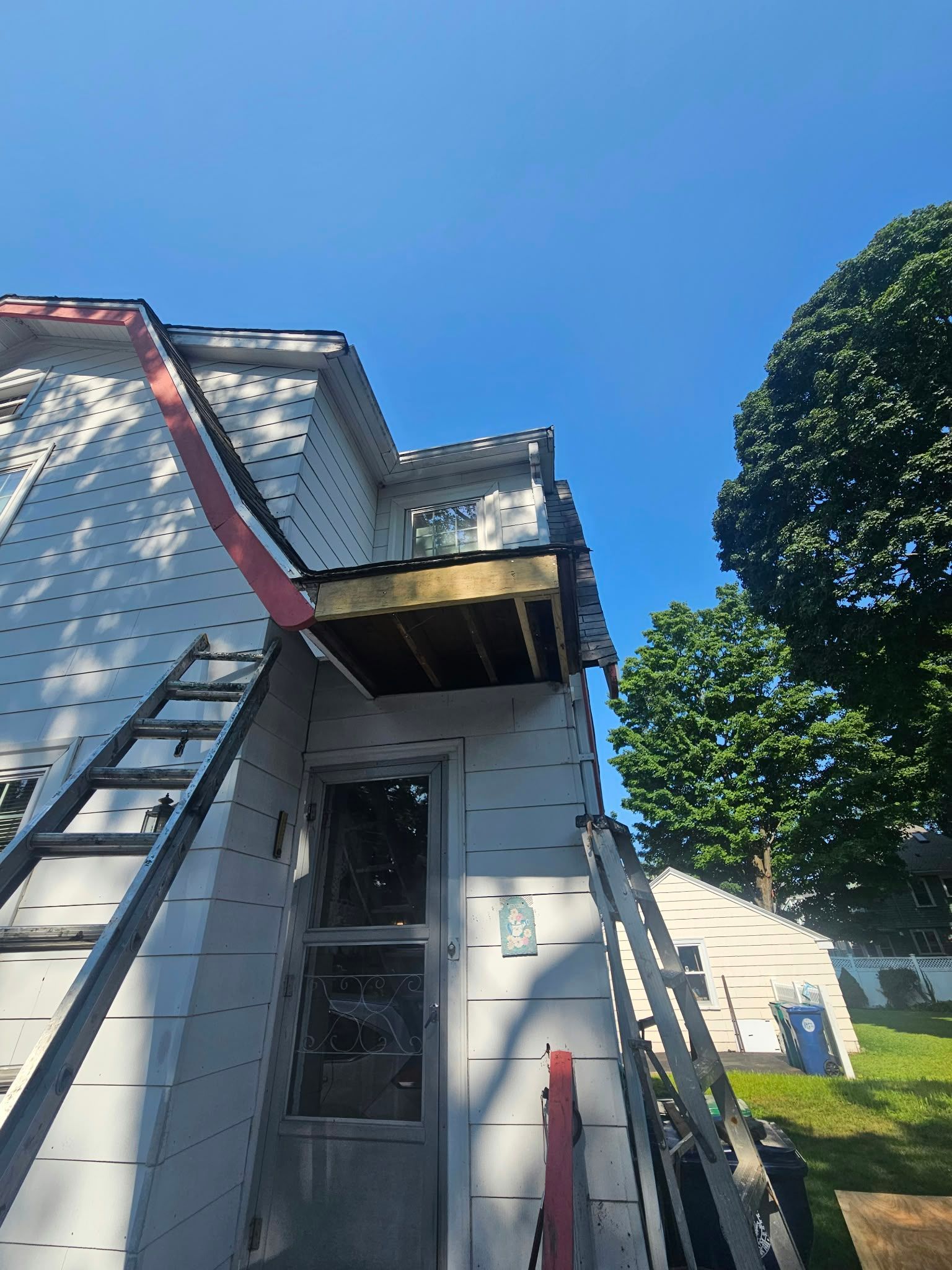 White house exterior with ladder and metal scaffold under a blue sky, tree and lawn beside it