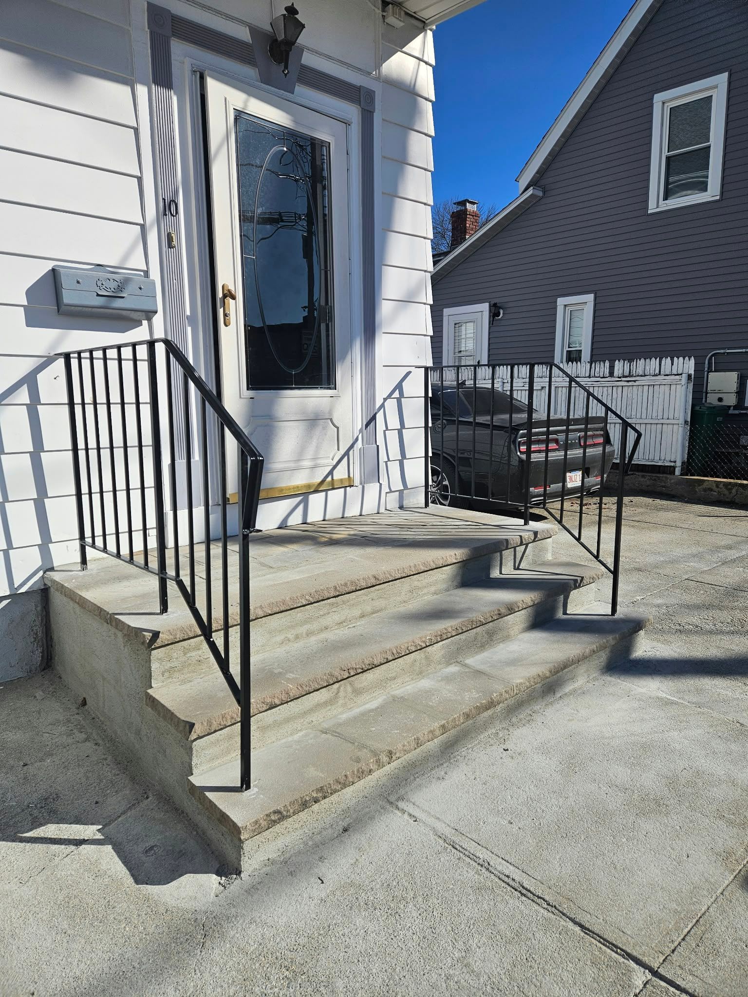 Front steps to a white house with a glass door and black railing, beside a neighboring gray house