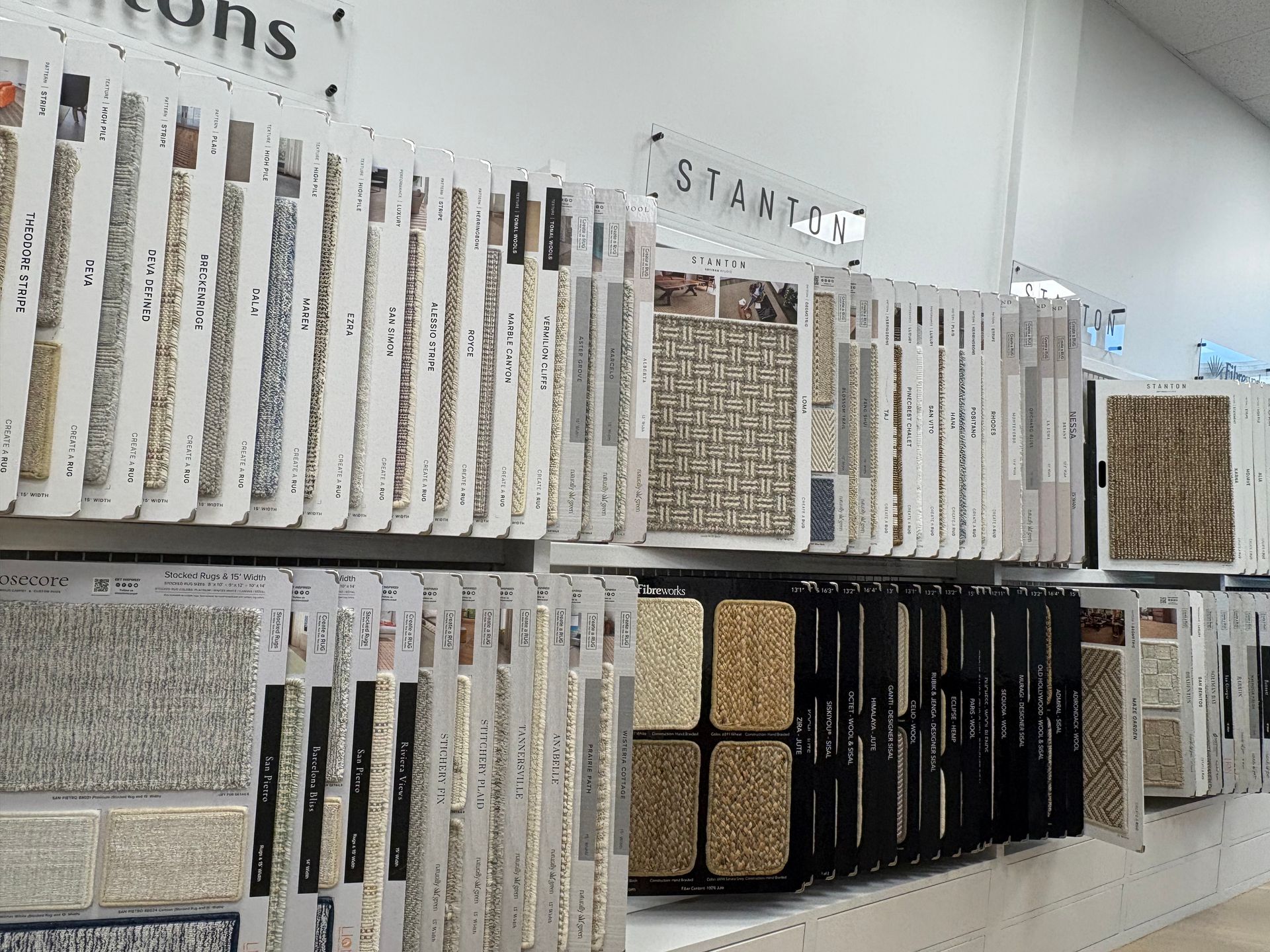 Display of carpet or tile samples on white shelves in a store, with neutral and dark swatches.