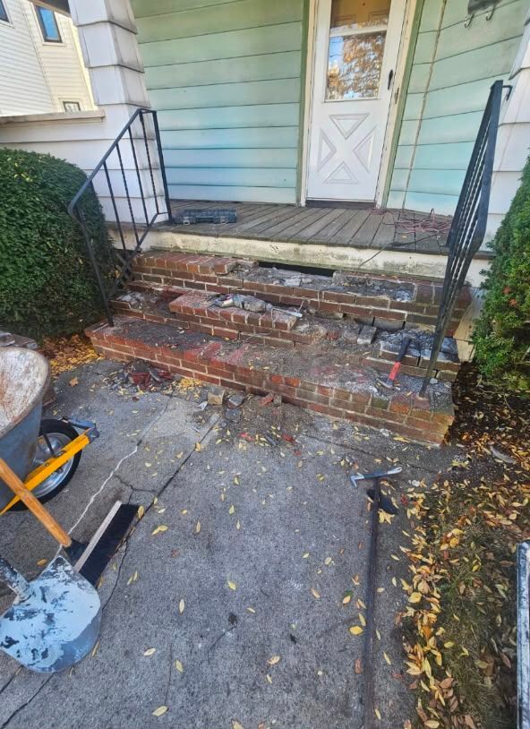Front steps with broken bricks, scattered debris, and a white door at a house entryway
