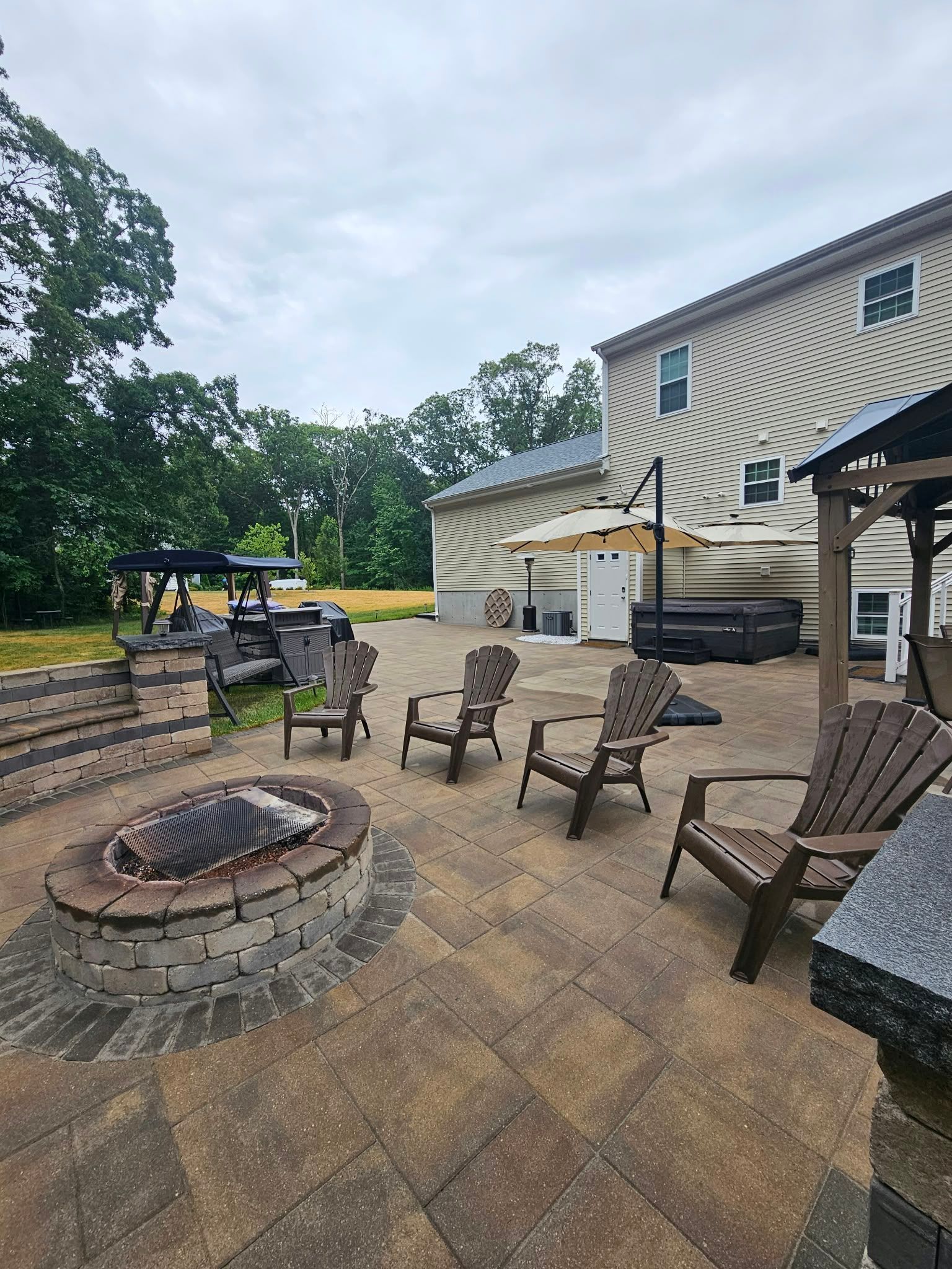 Patio with fire pit and wooden chairs beside a striped house on a cloudy day