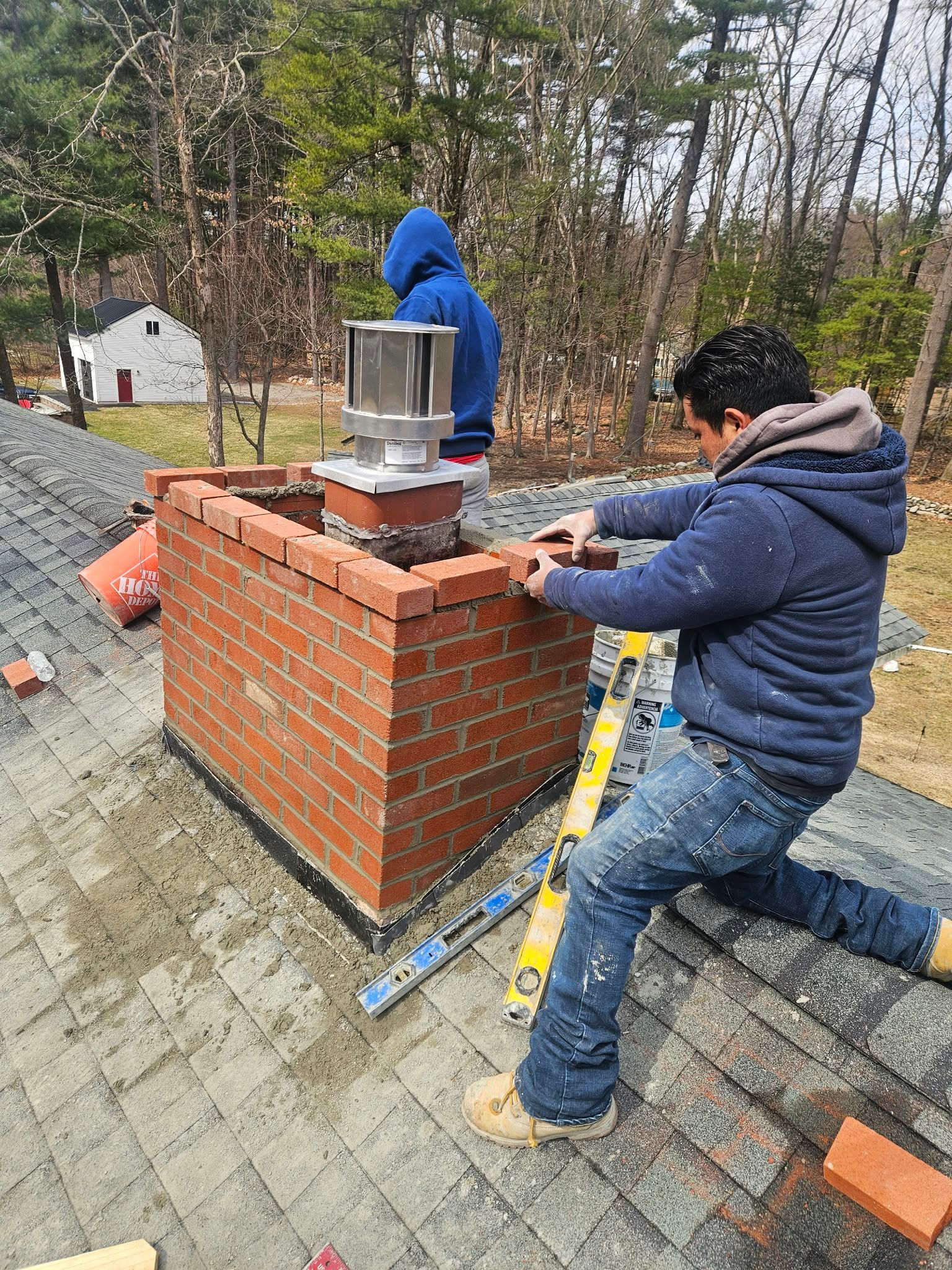 Two workers installing a metal chimney on a brick structure outdoors.