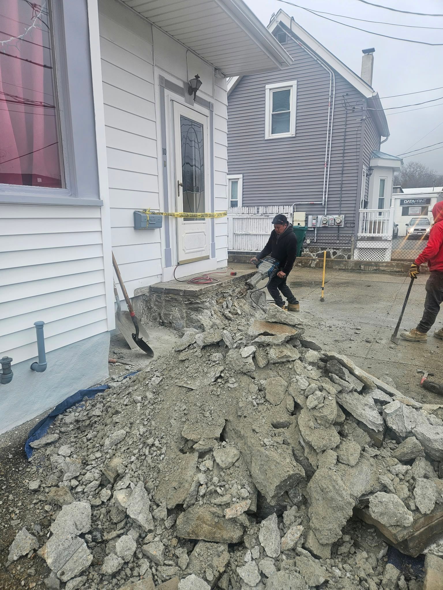 Worker near caution tape beside a damaged house and large pile of broken concrete rubble