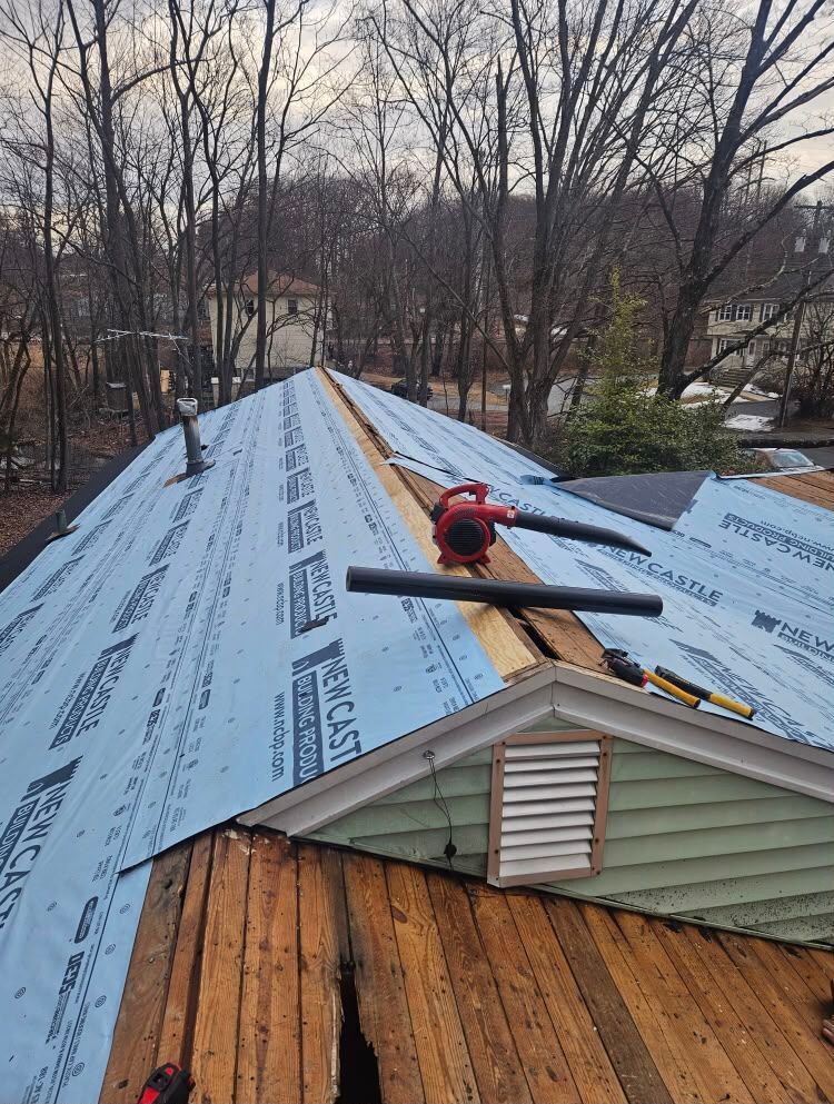 Workers reroofing a house with blue underlayment and bare wood decking visible at the front edge.