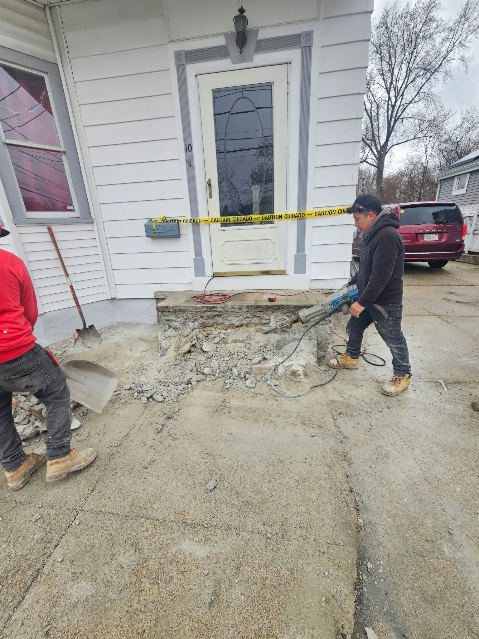 Workers shovel muddy dirt at a house entrance blocked by caution tape after damage or construction.