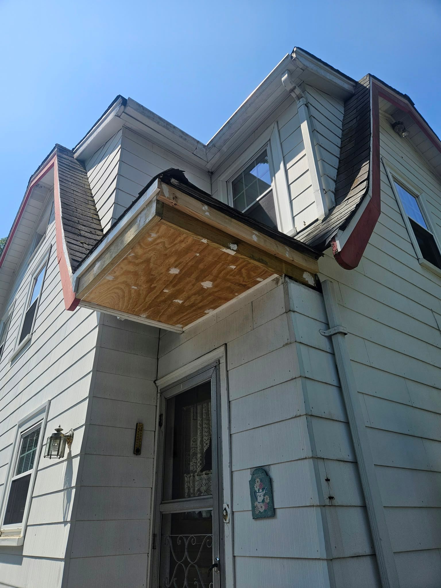 Front entrance of a house with a small wood-paneled awning and vinyl siding, viewed from below