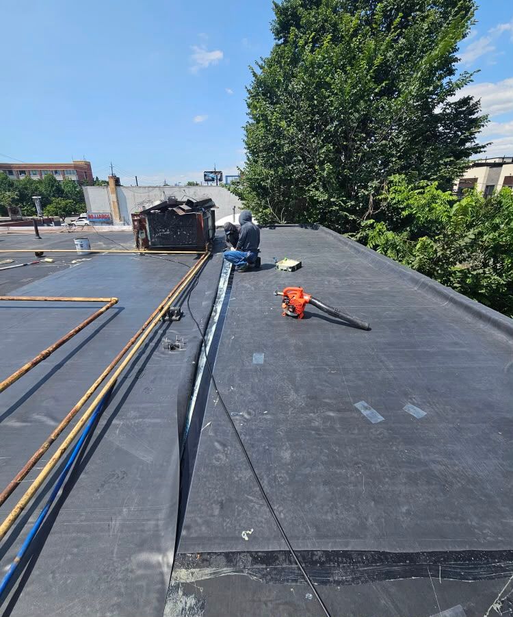 Rooftop construction site with black roofing membrane, tools, and materials under a blue sky.