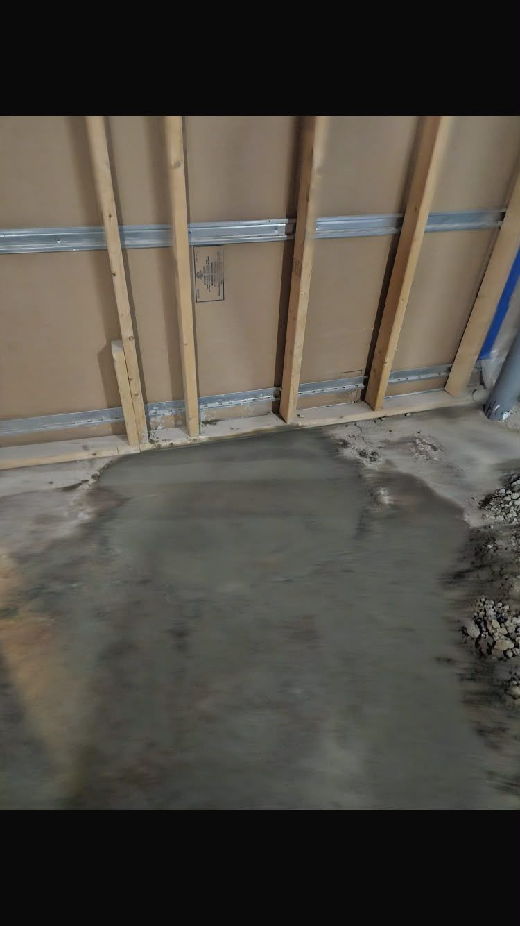 Concrete floor in front of a tan garage door with a small wet patch near the bottom.