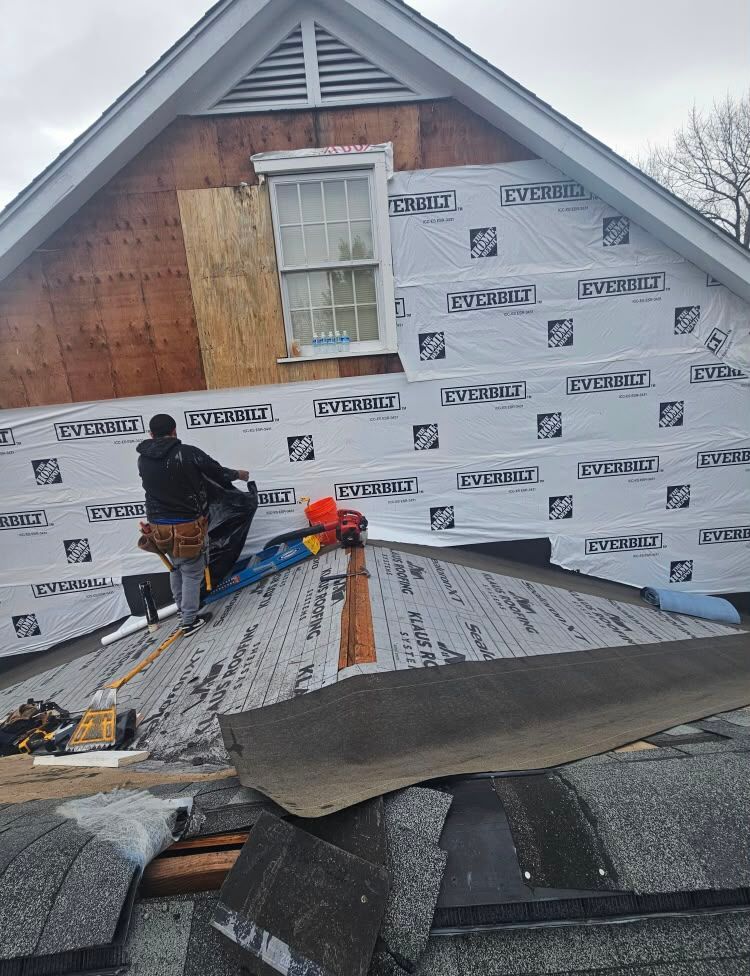 Workers installing roofing on a house with gray underlayment and white siding