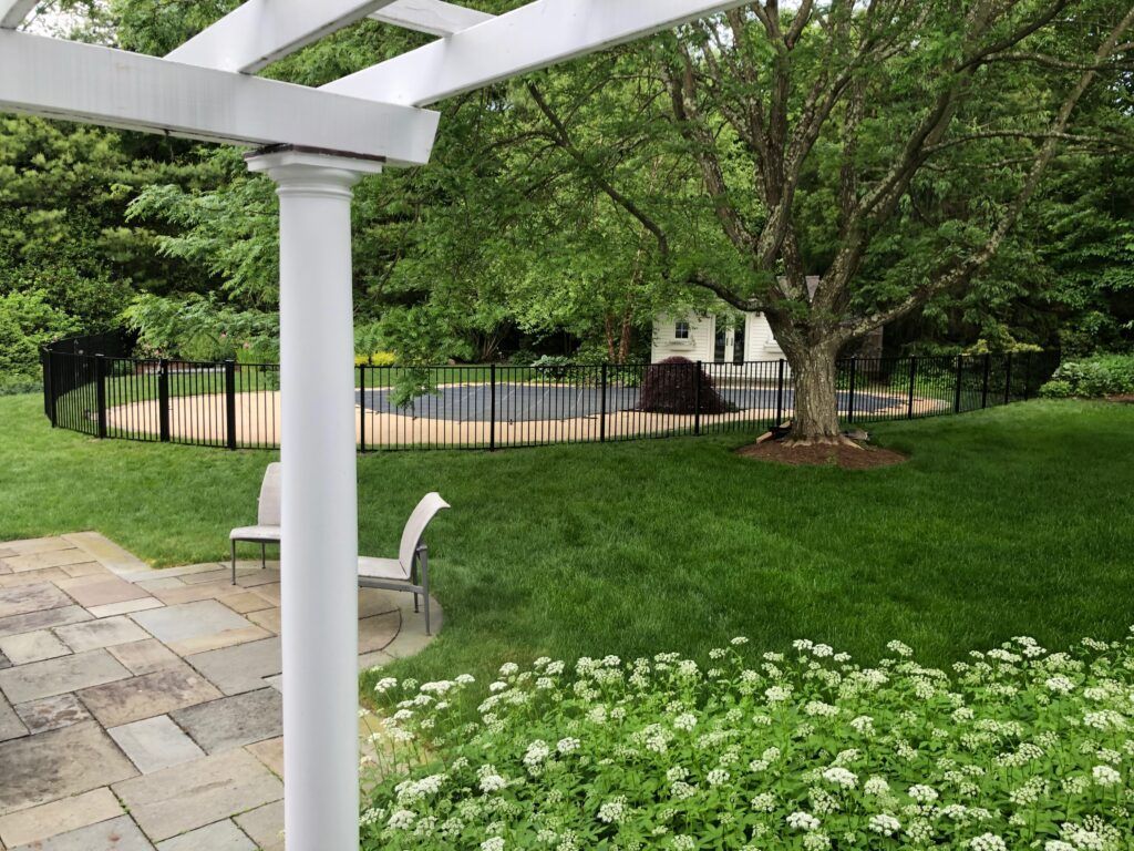 A white pergola overlooking a lush green yard with a pool in the background.