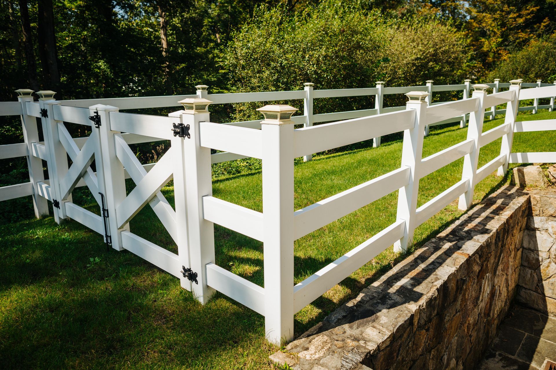 A white fence with a gate is surrounded by grass and trees.