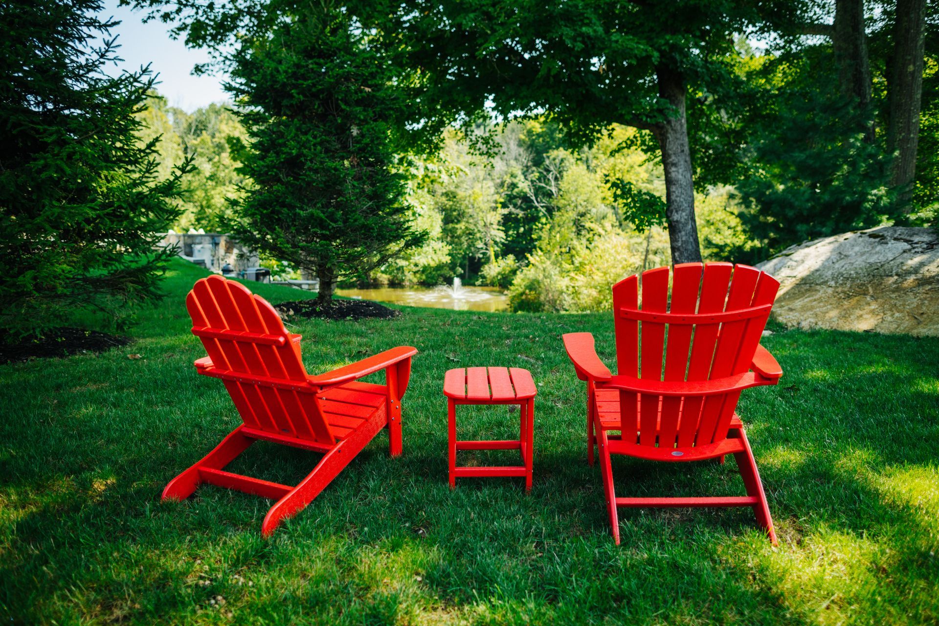 Two red adirondack chairs and a small table are sitting on a lush green lawn.