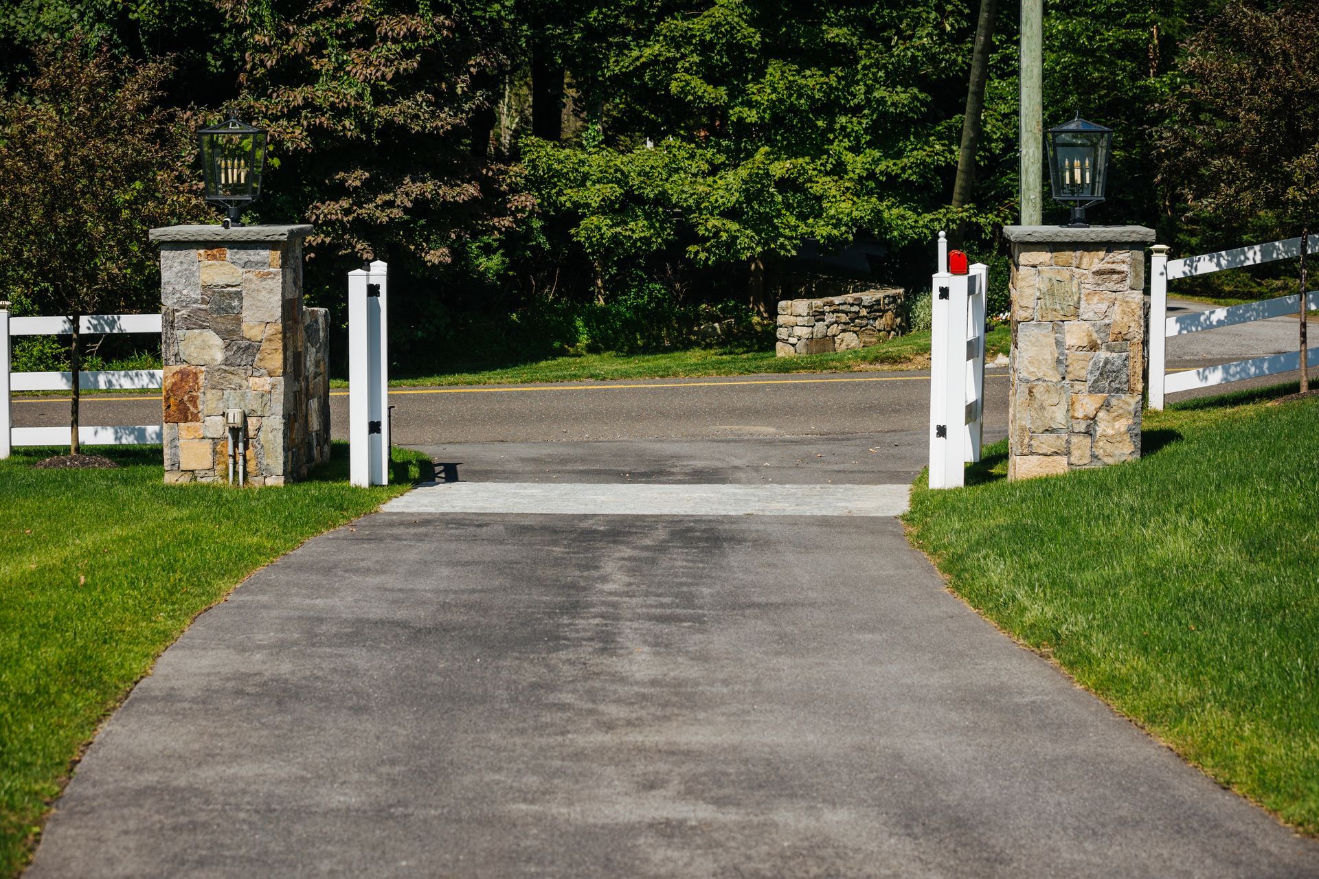 A driveway leading to a stone gate with a white fence in the background.