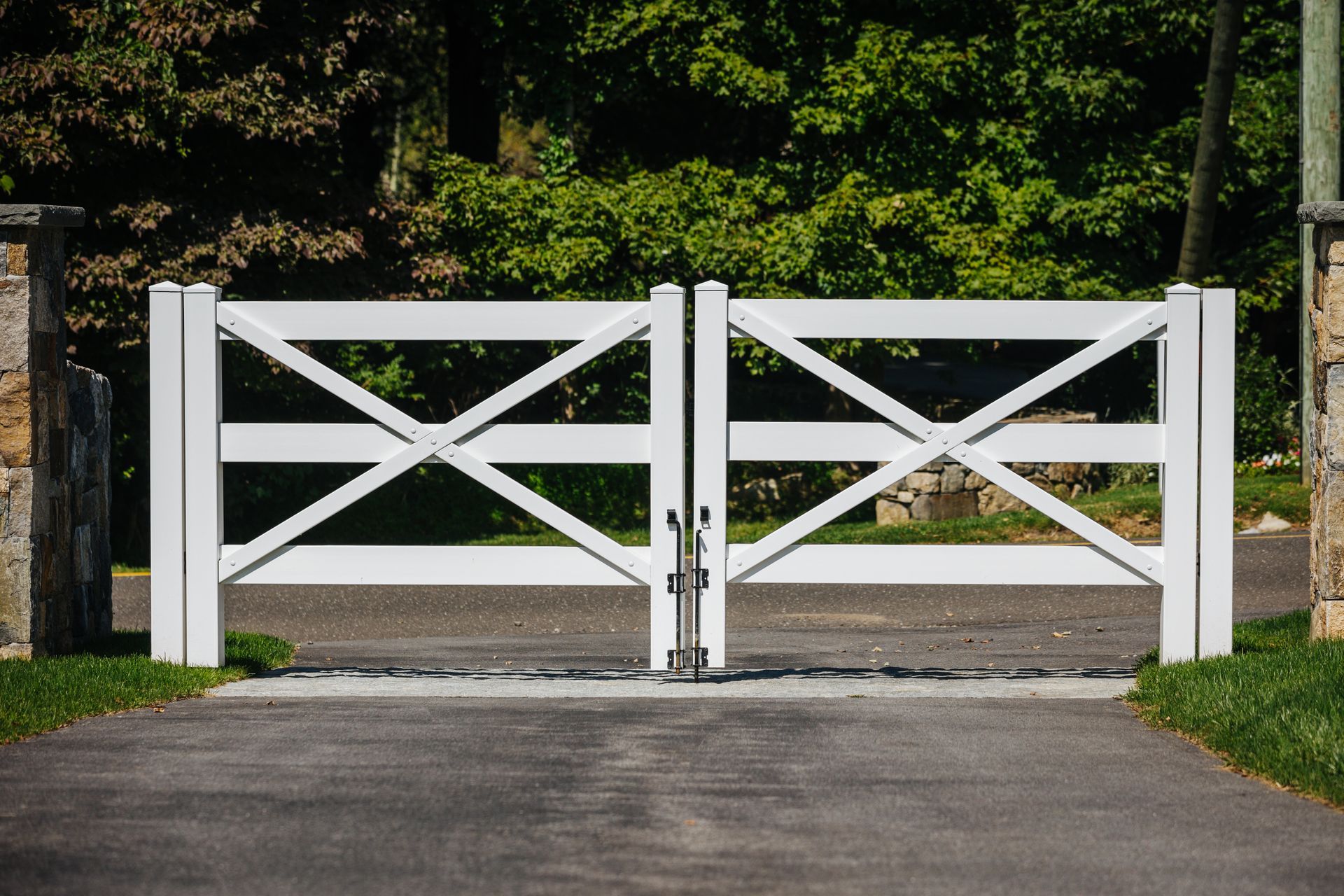 A white gate is open to a driveway with trees in the background