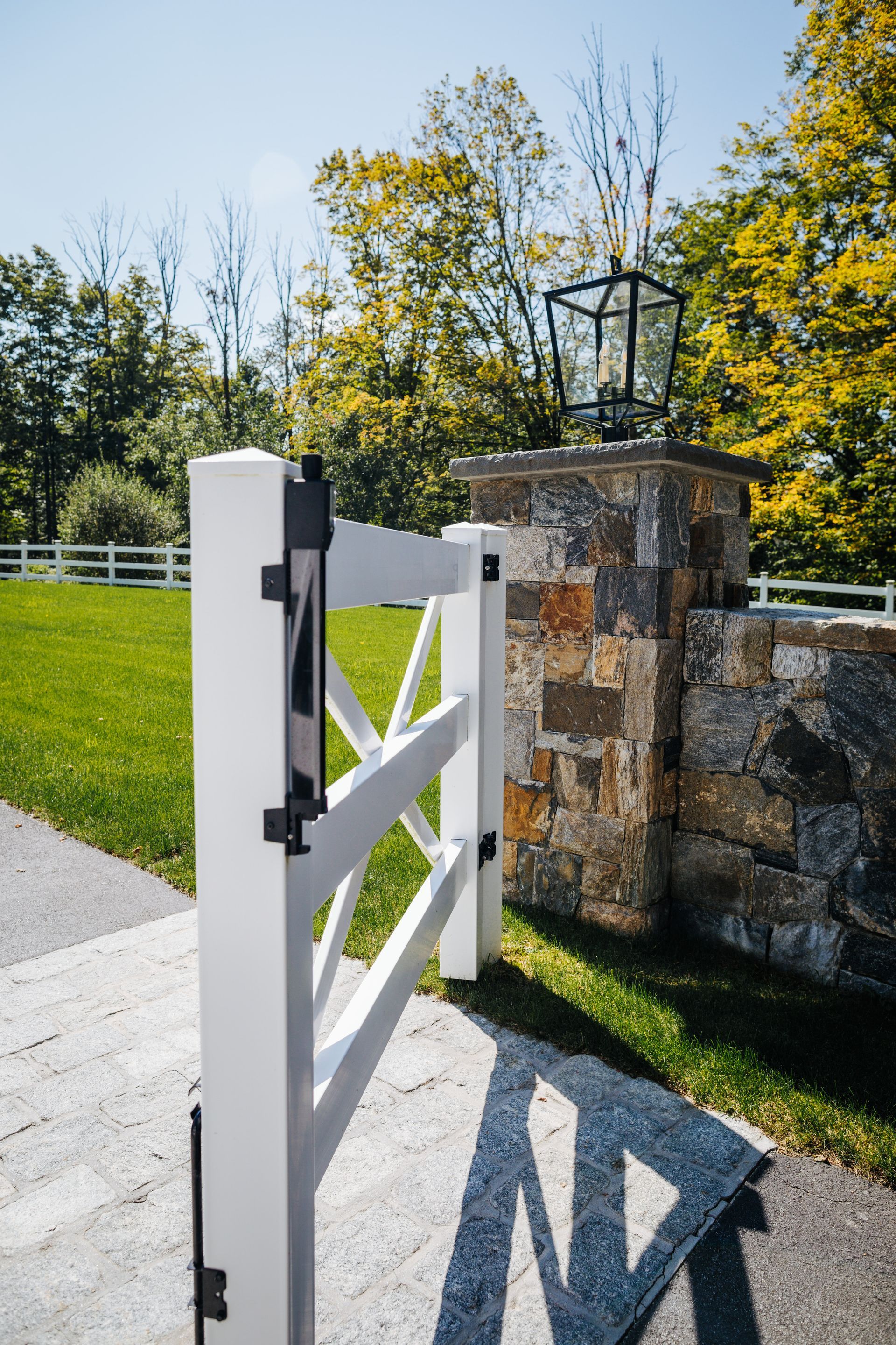 A white gate is sitting on the side of a road next to a stone wall.