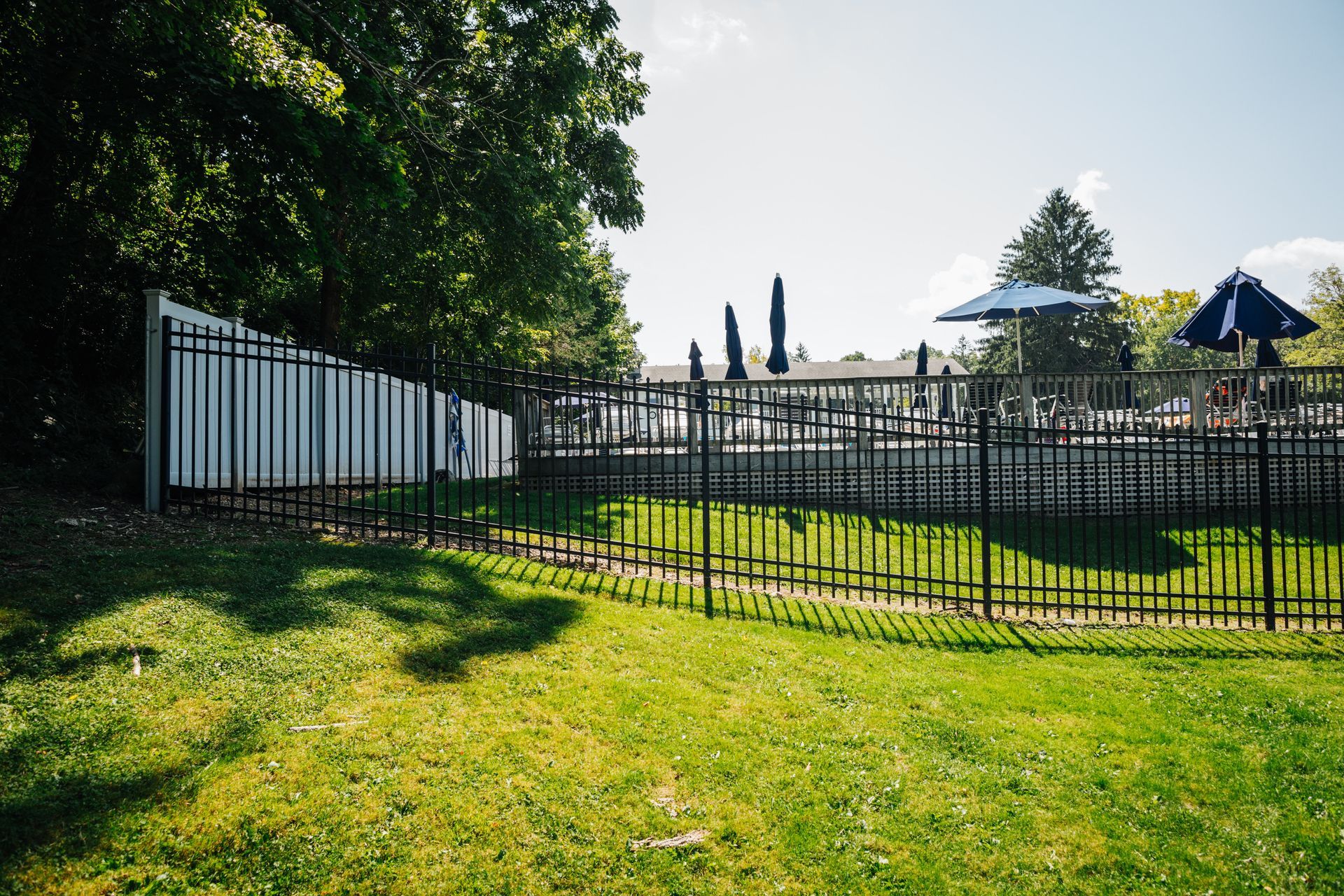 A fence surrounds a lush green field with a swimming pool in the background.