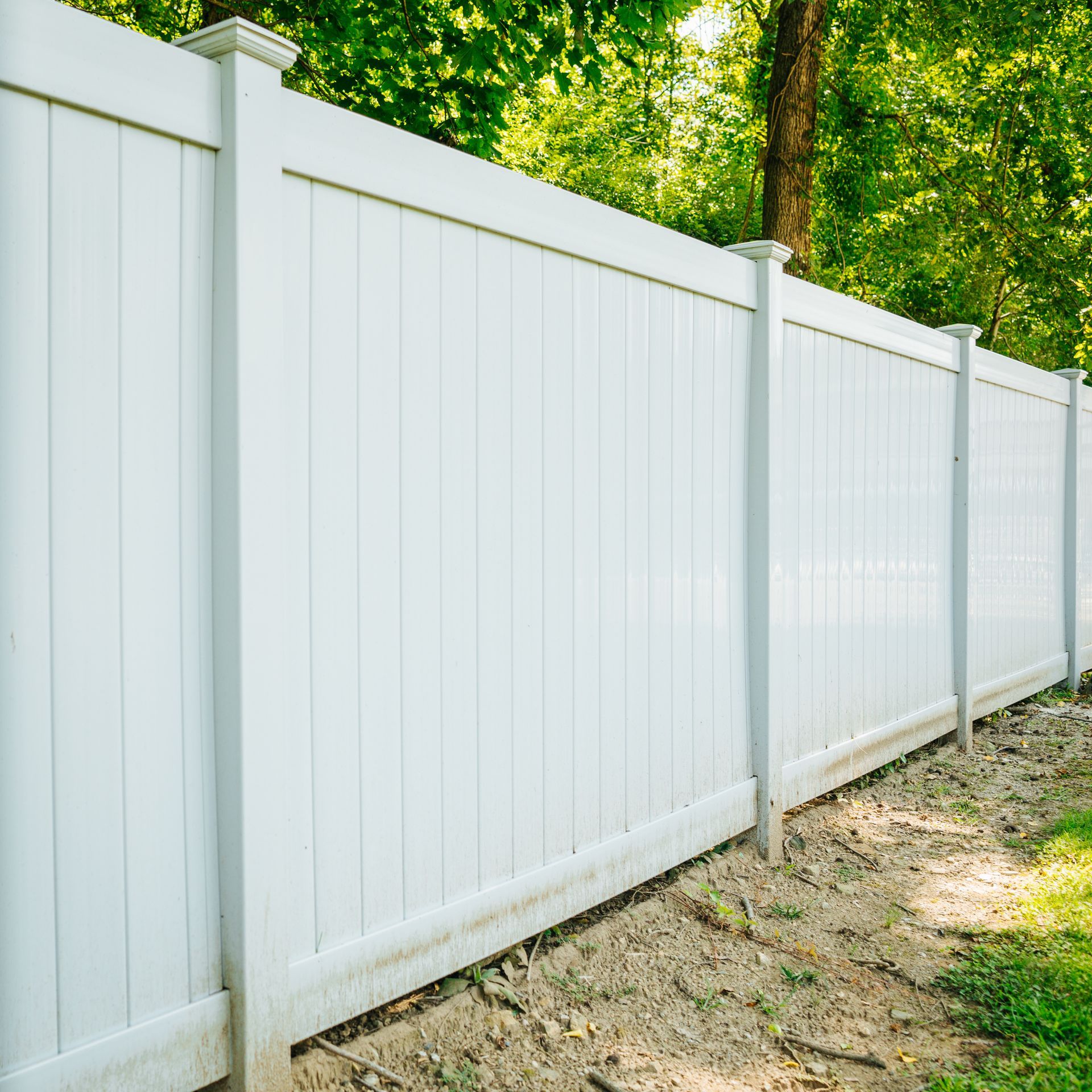 A white fence is surrounded by trees and dirt.