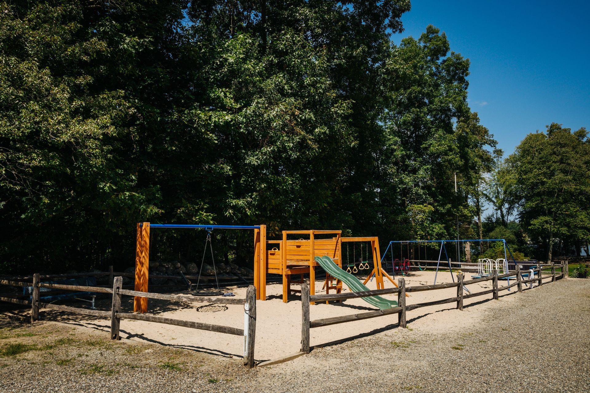 A playground with a wooden fence and trees in the background.