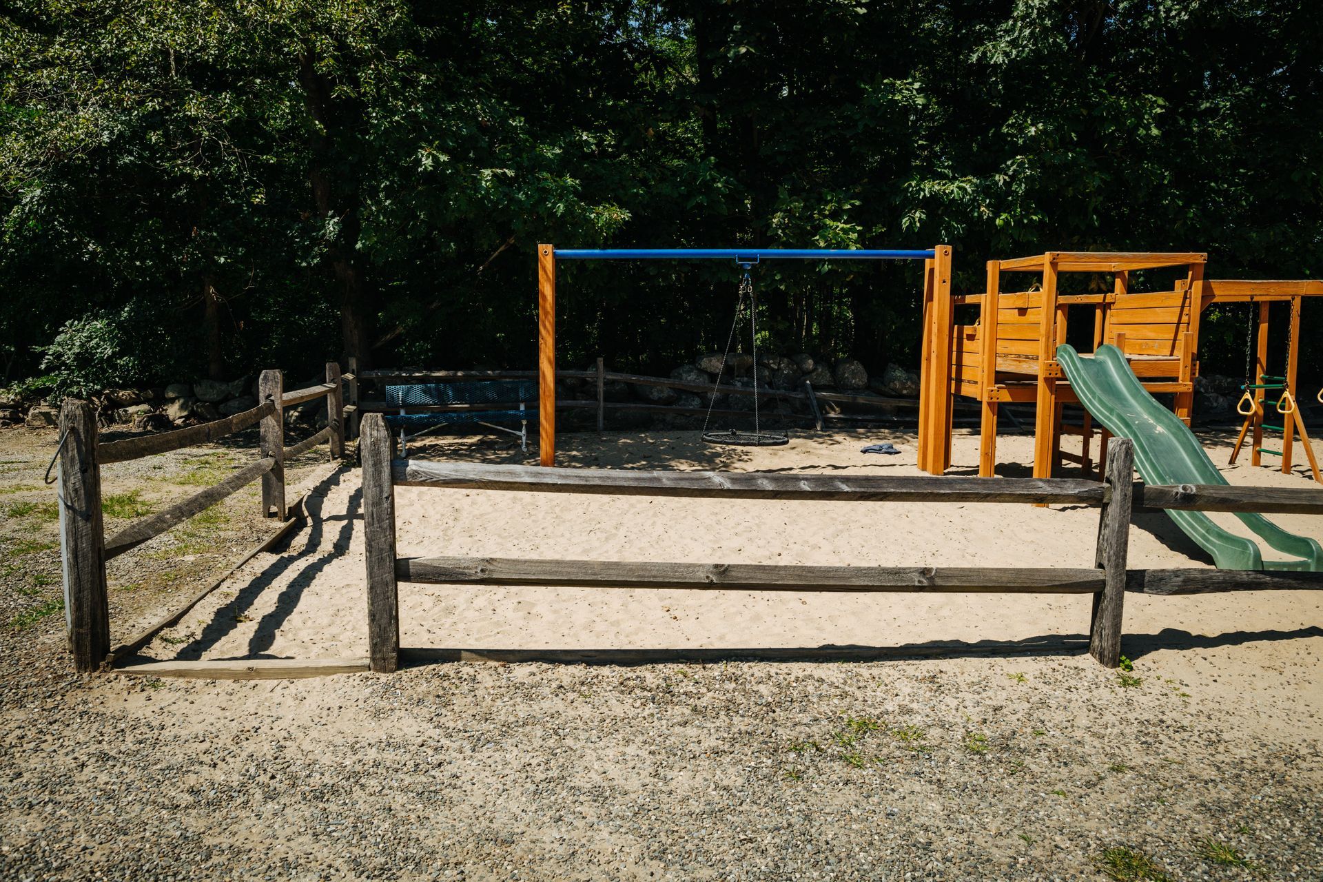 A playground with a wooden fence and swings and a slide.