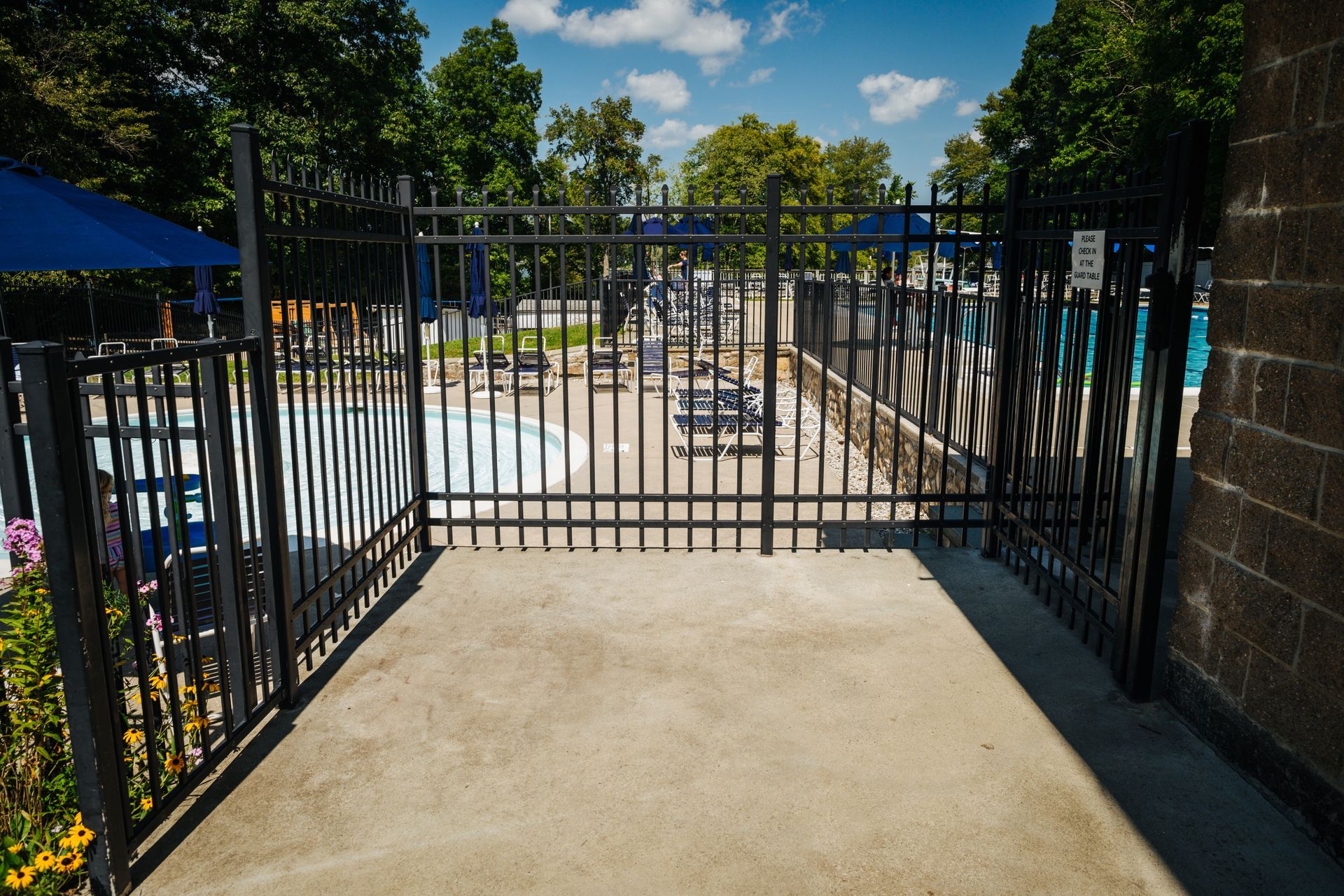 A metal gate leading to a swimming pool with a brick wall in the background.