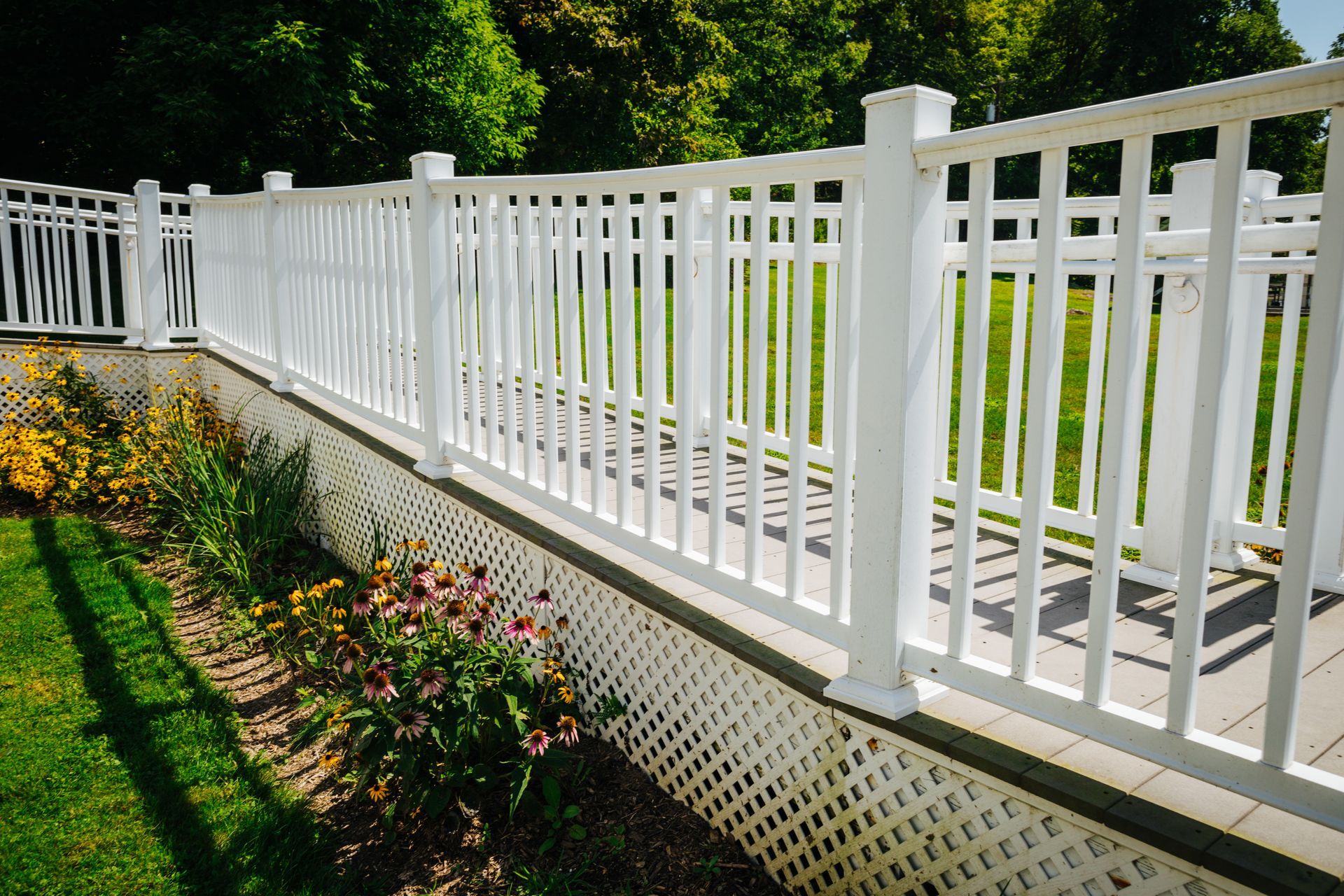 A white fence surrounds a garden with flowers and grass.