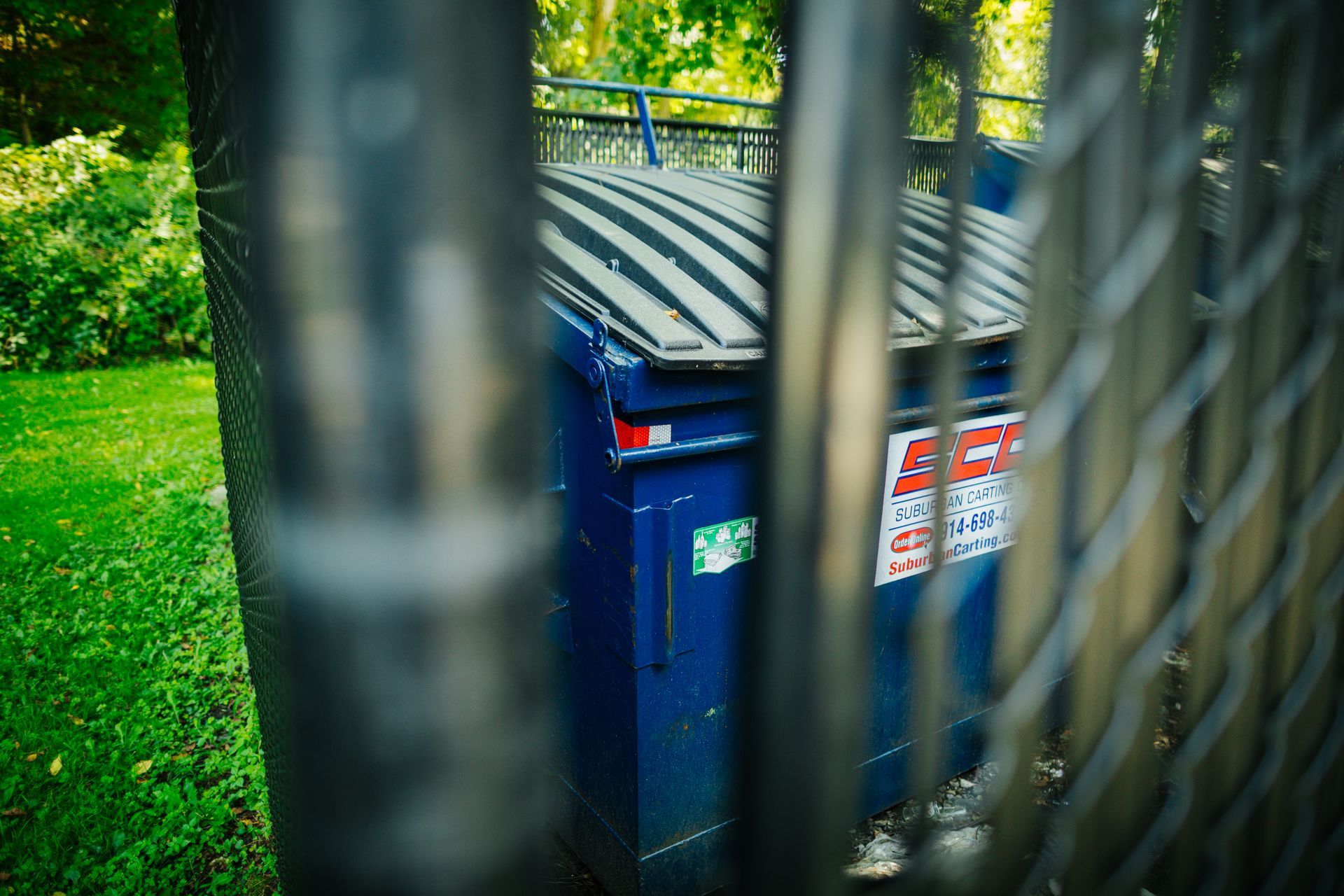 A blue dumpster is behind a chain link fence.