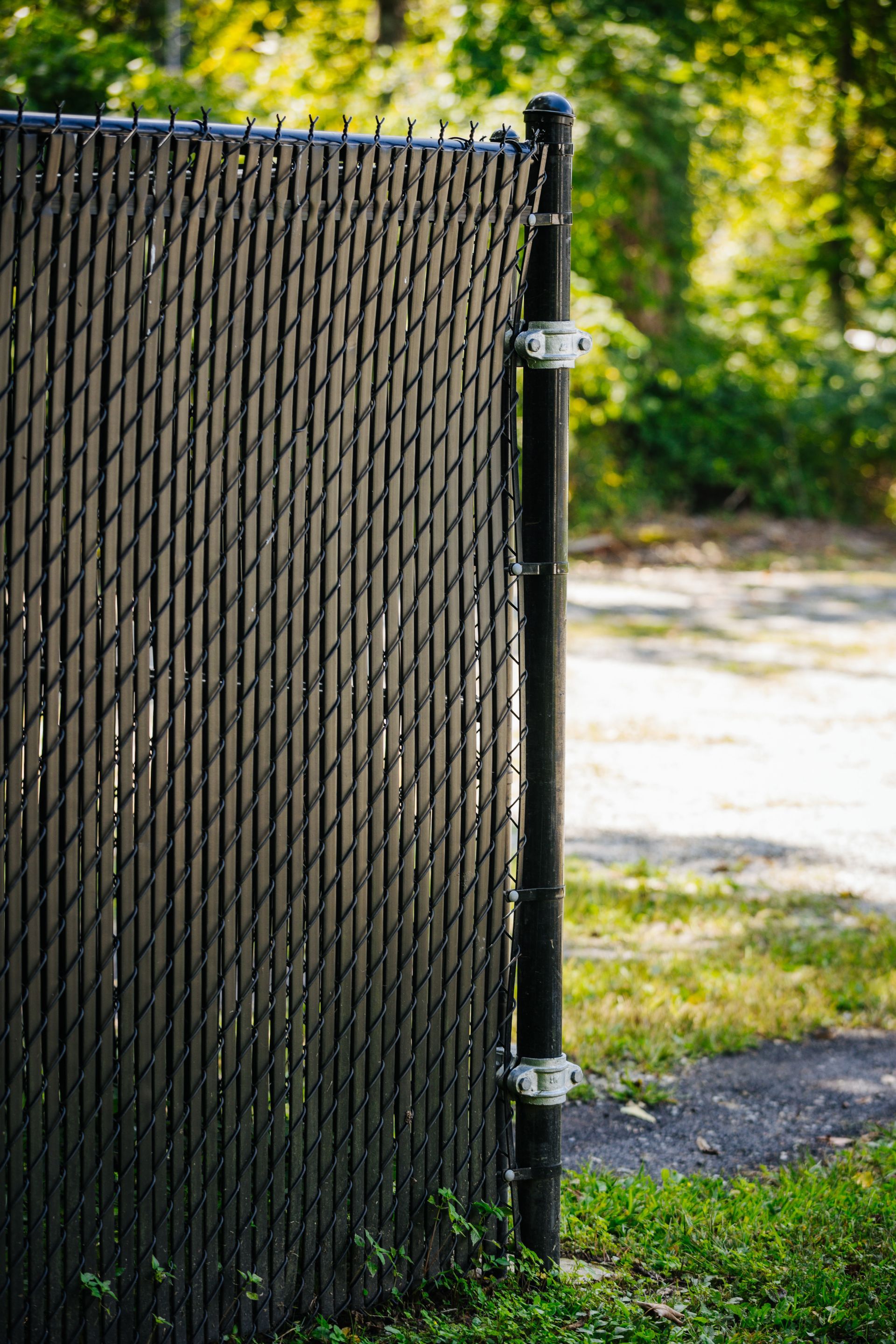 A black chain link fence is sitting in the grass next to a dirt road.