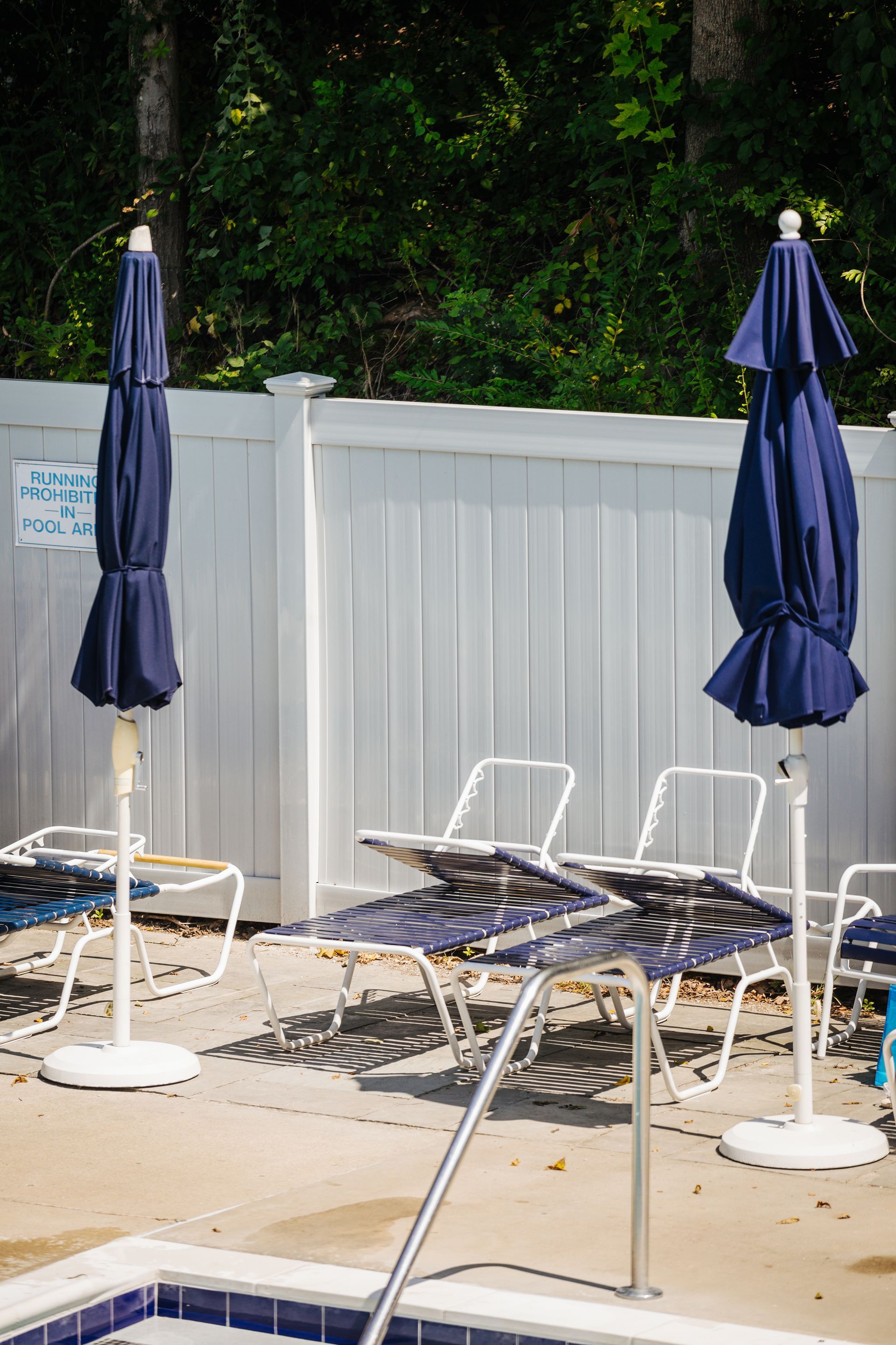 A swimming pool with chairs and umbrellas in front of a white fence.
