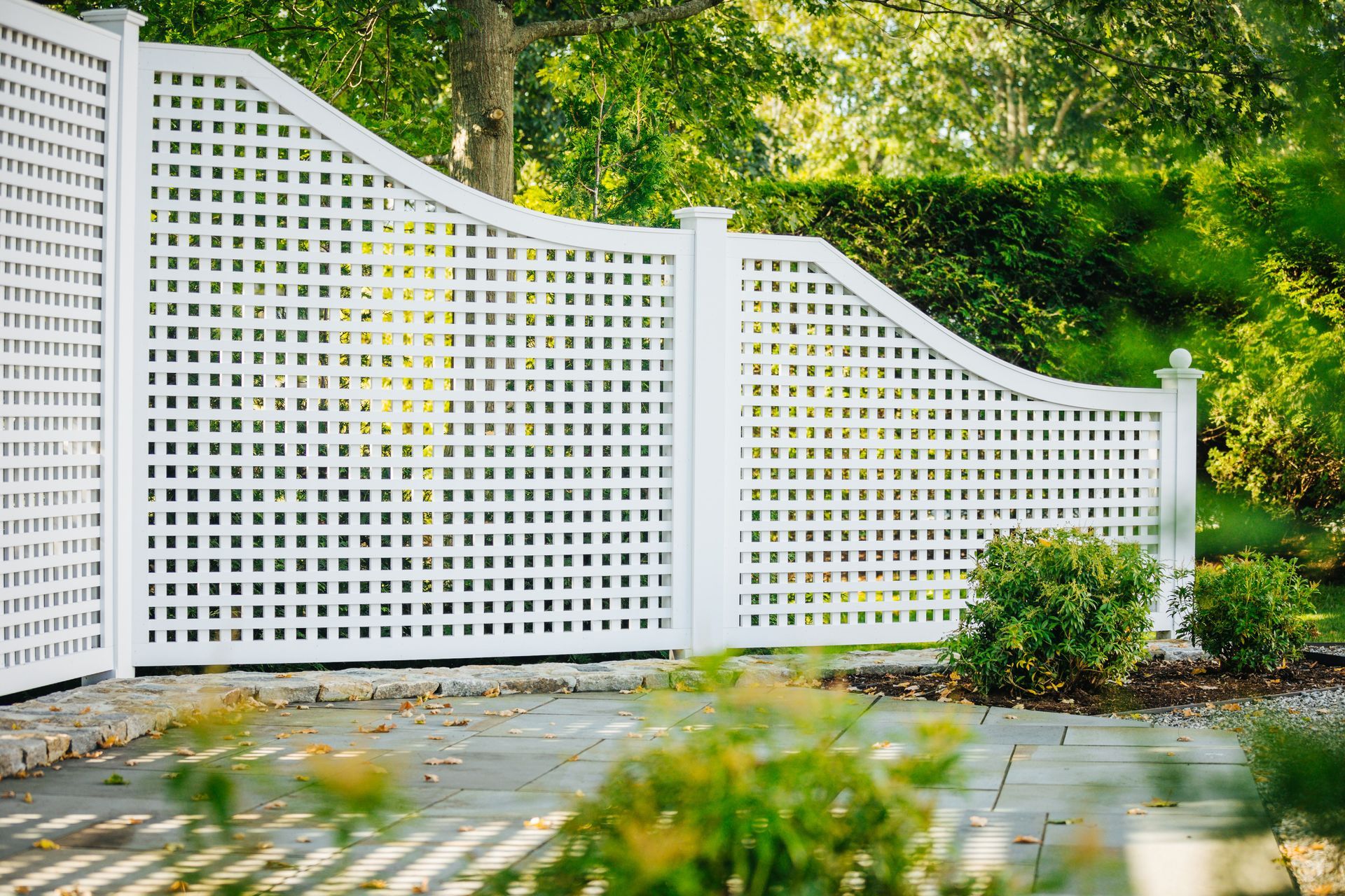 A white lattice fence is surrounded by trees and bushes.