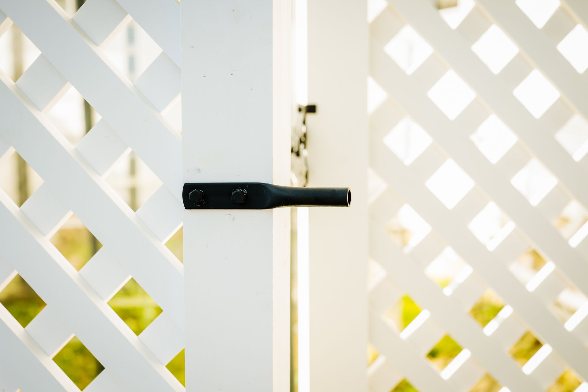 A close up of a white lattice fence with a black handle.