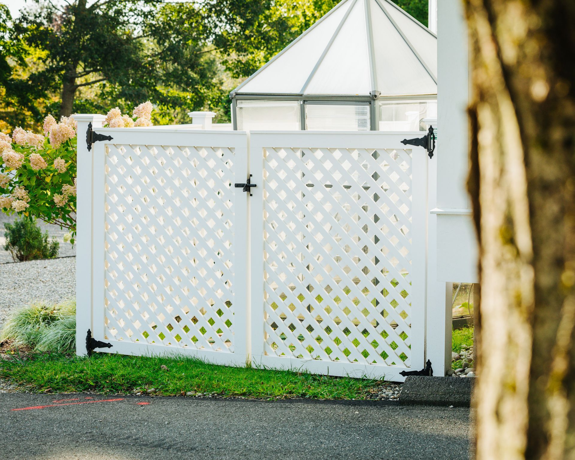 A white lattice fence with a gate and a gazebo in the background