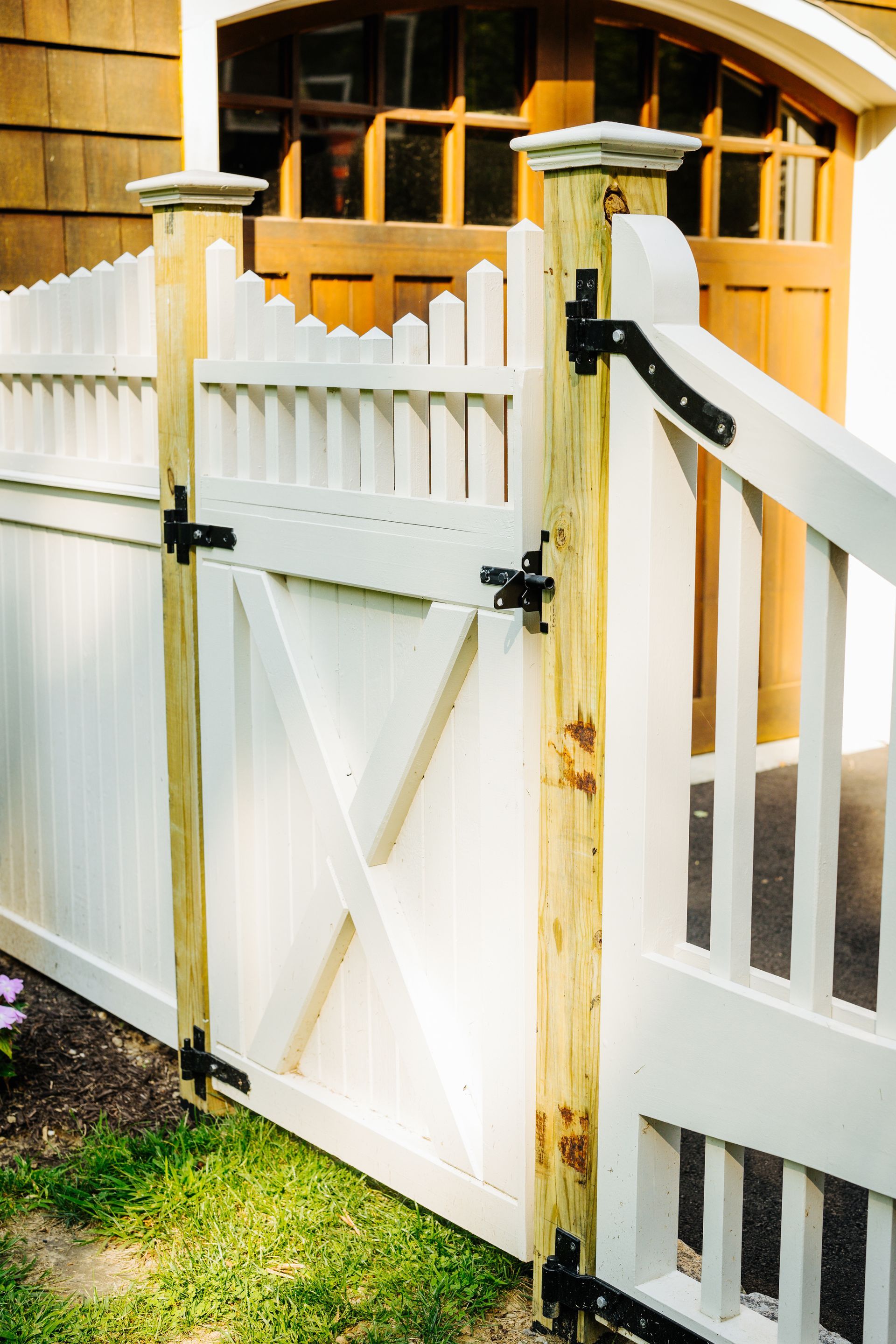 A white fence with a wooden gate in front of a garage door