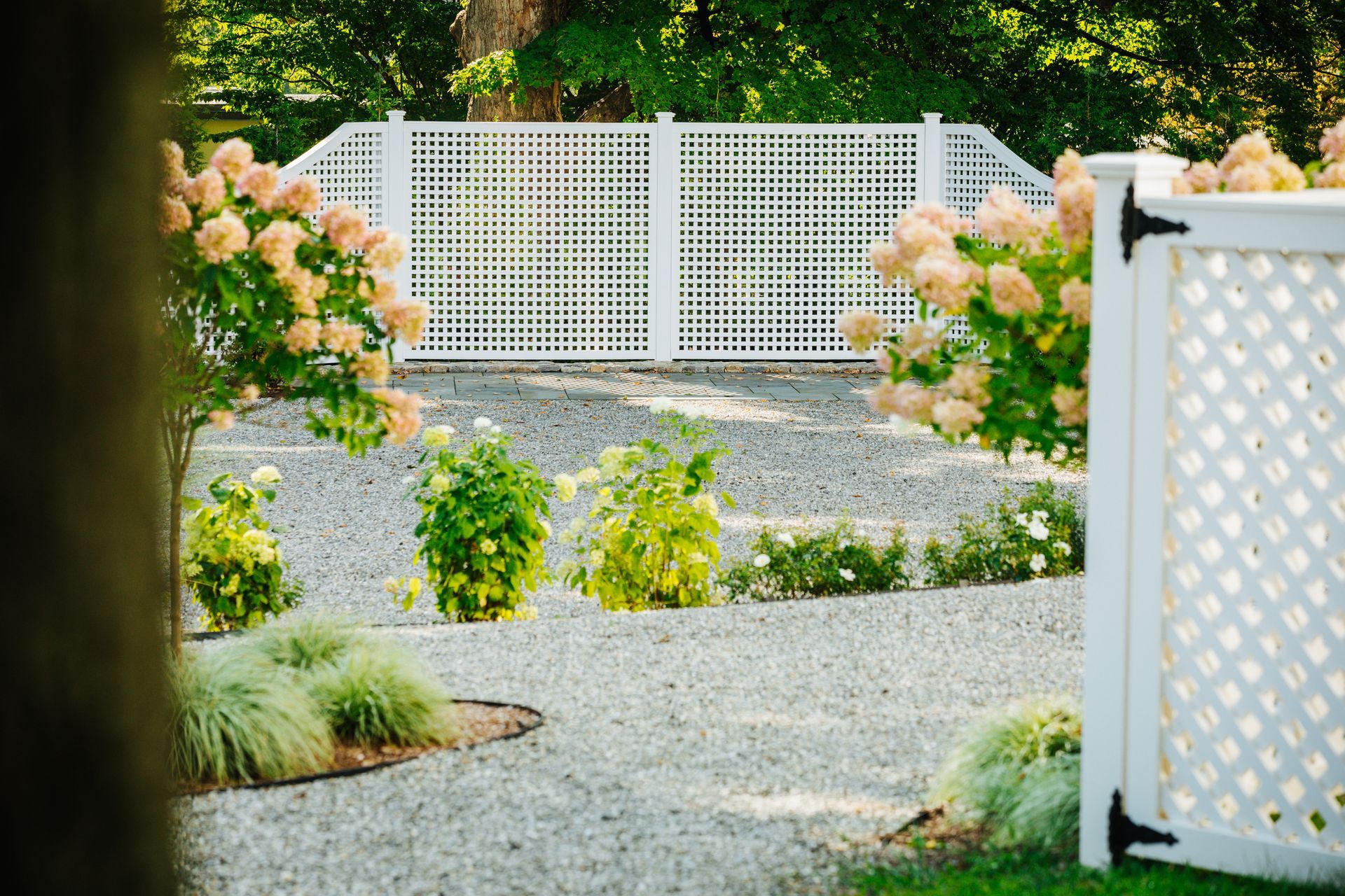 A white lattice fence surrounds a gravel driveway in a garden.