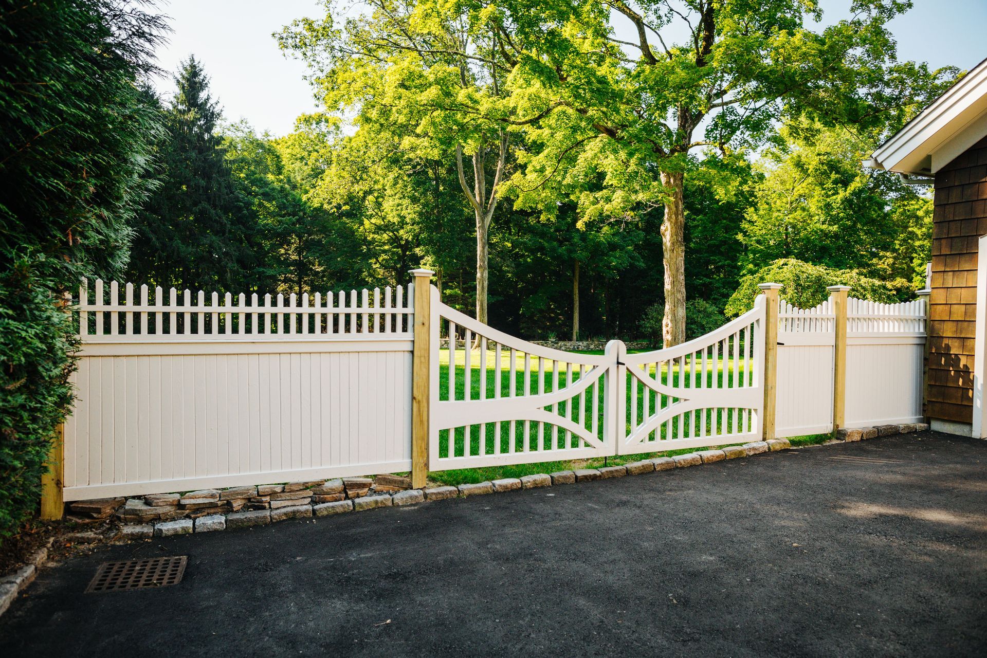 A white fence is surrounding a driveway with trees in the background.